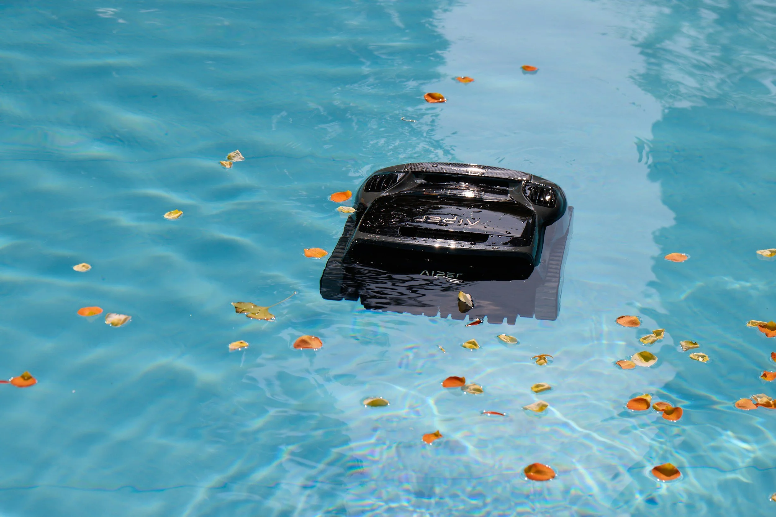 A black robotic pool cleaner submerged in a swimming pool, surrounded by floating leaves.
