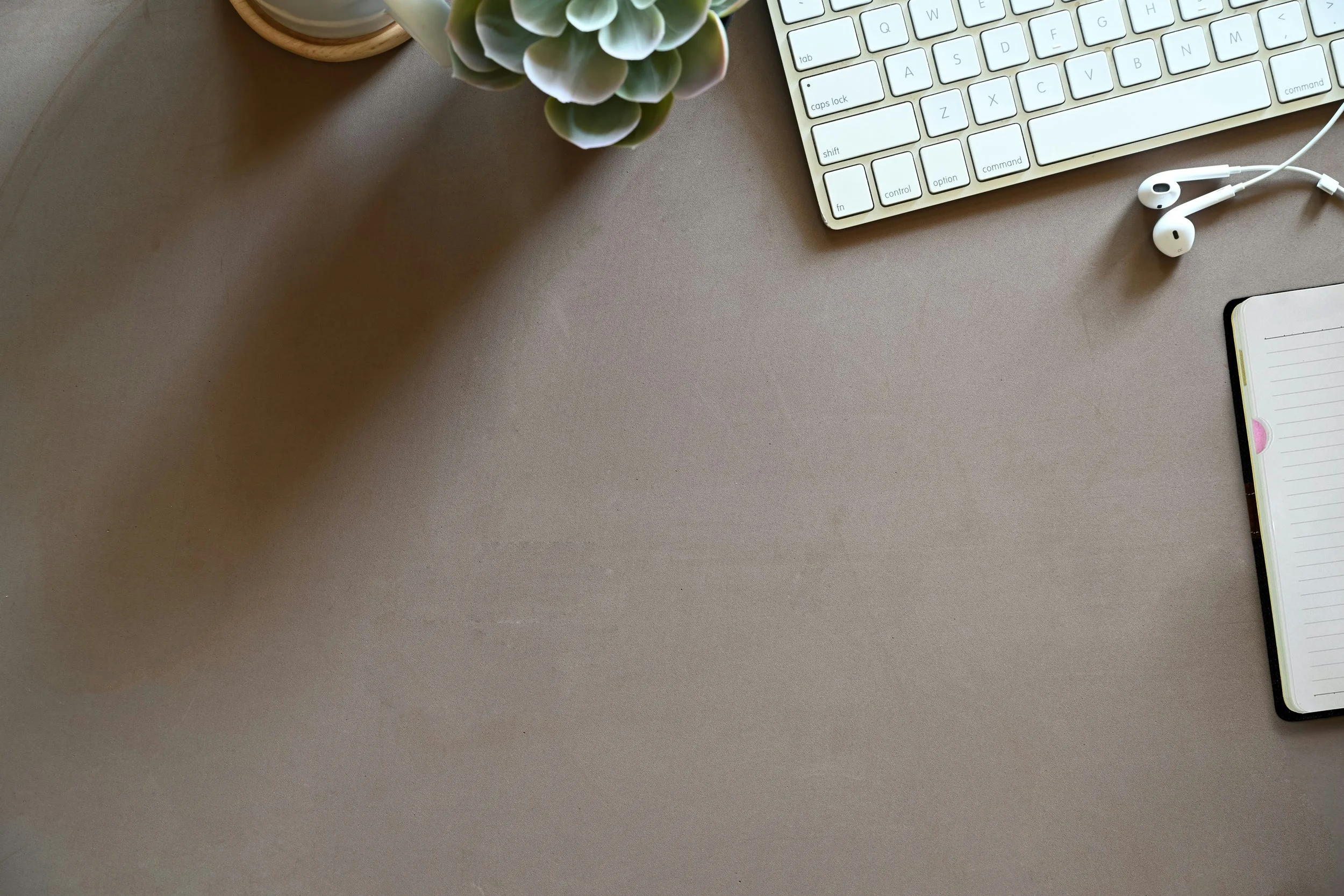 A computer keyboard, a smartphone with a notepad, a pair of white earphones, a succulent plant in a pot, all placed on a beige desk.