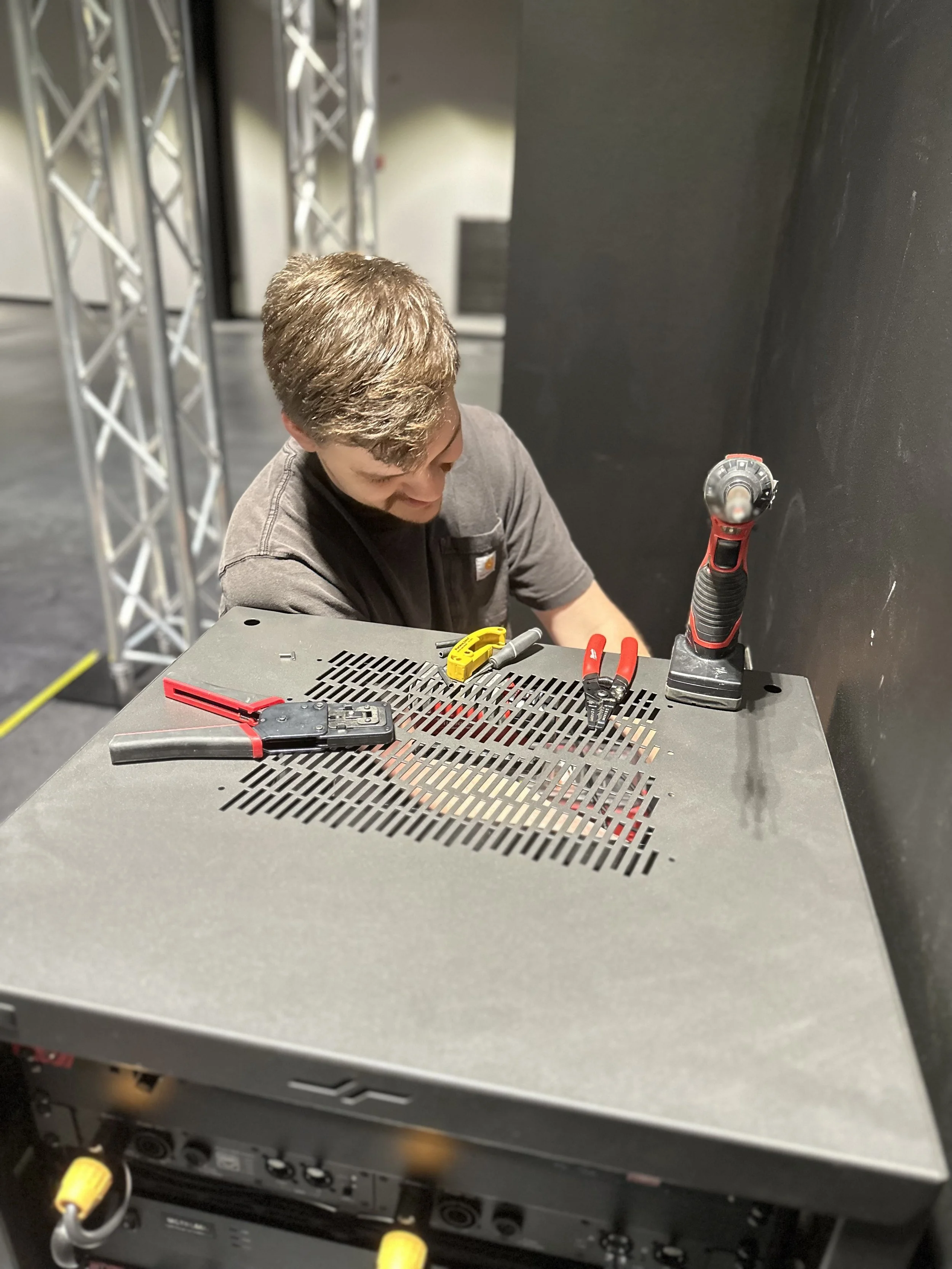 A man working on electronic equipment with tools on a metallic table in a workshop or stage setup.