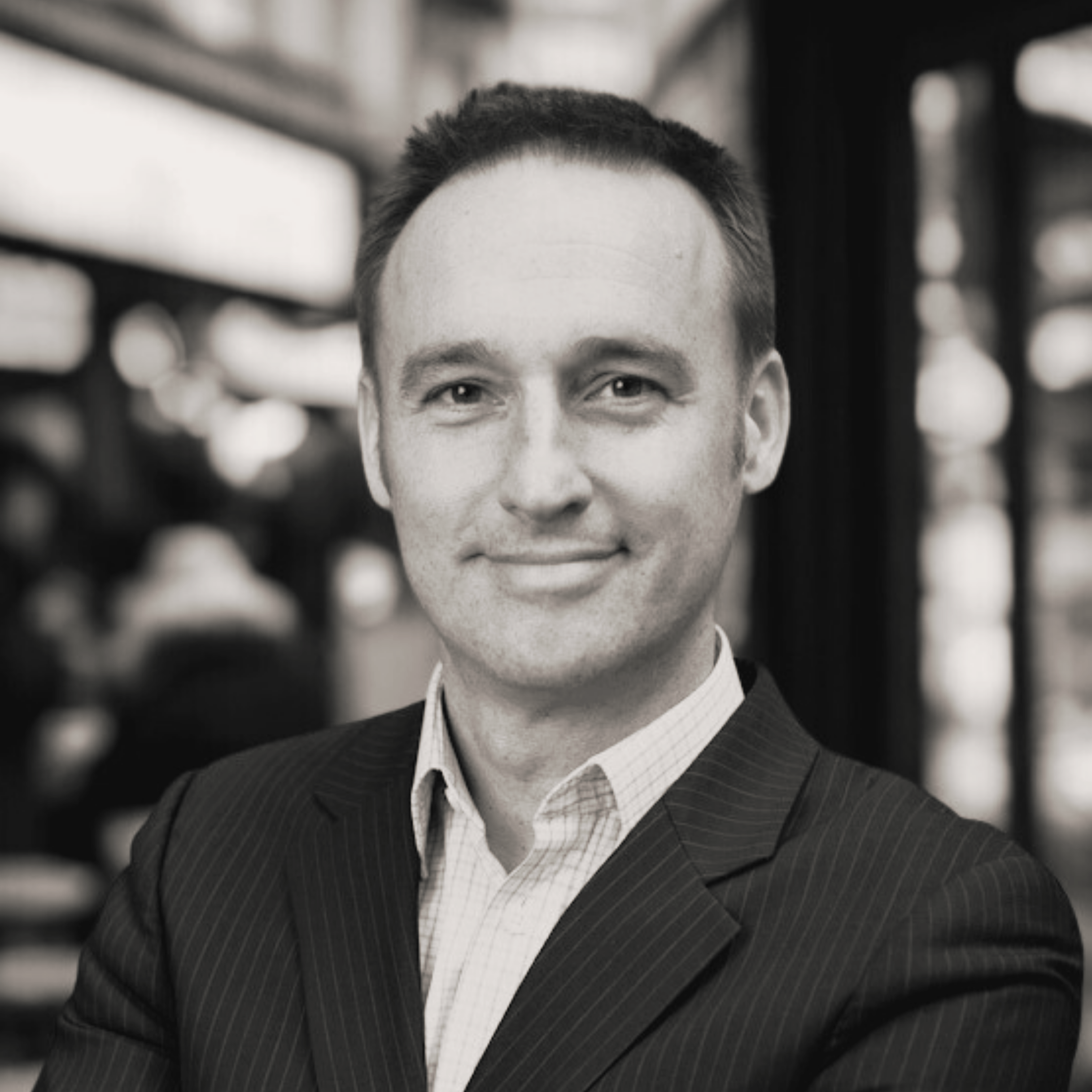 Black and white portrait of a smiling man in a suit with a collared shirt, standing indoors with blurred background.