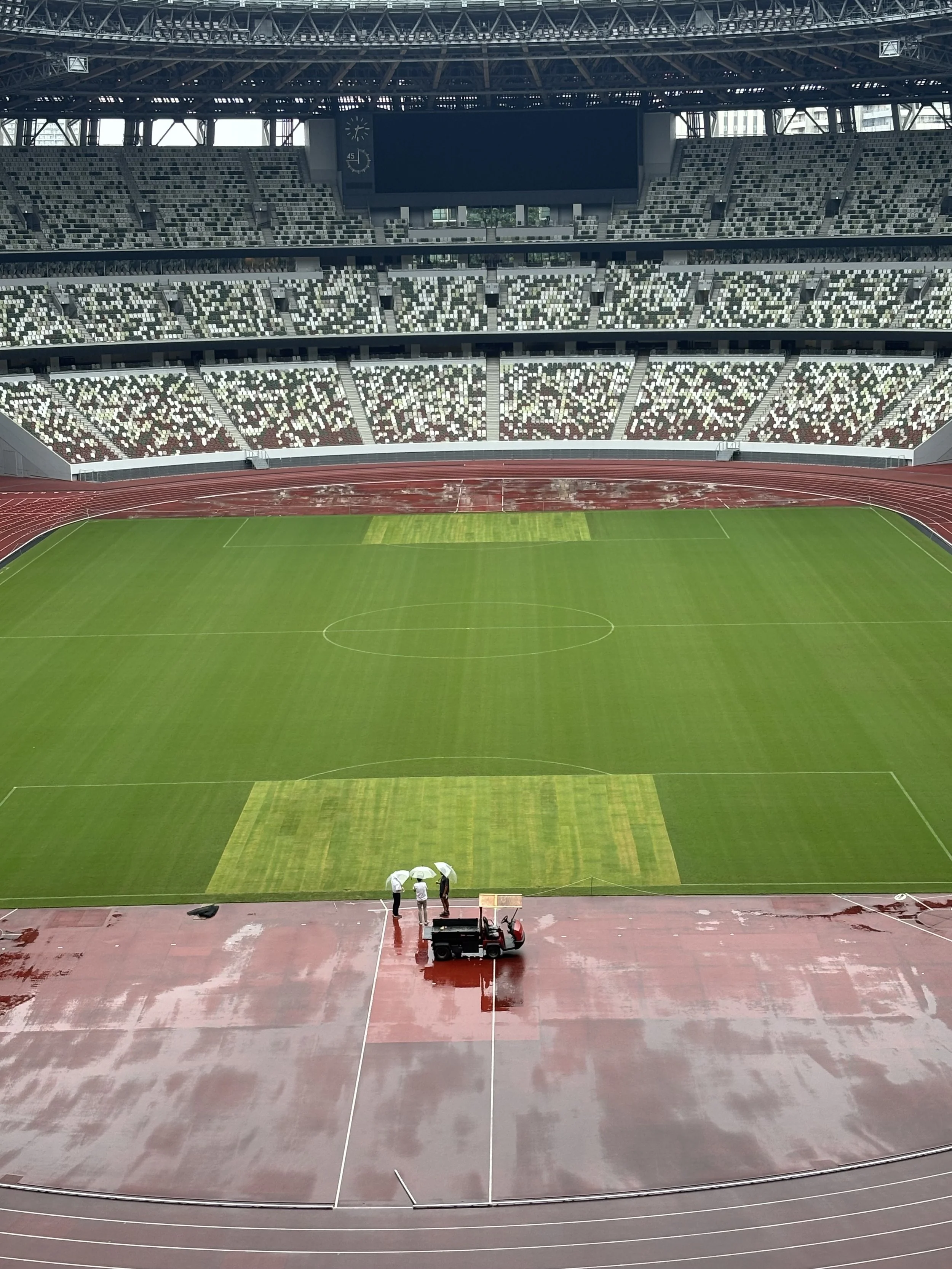 A photo taken from the inside of the Tokyo 2020 olympic stadium now known as the MUFG National Stadium. Photo taken from up high looking down on the field and showing the three tiers of seating.