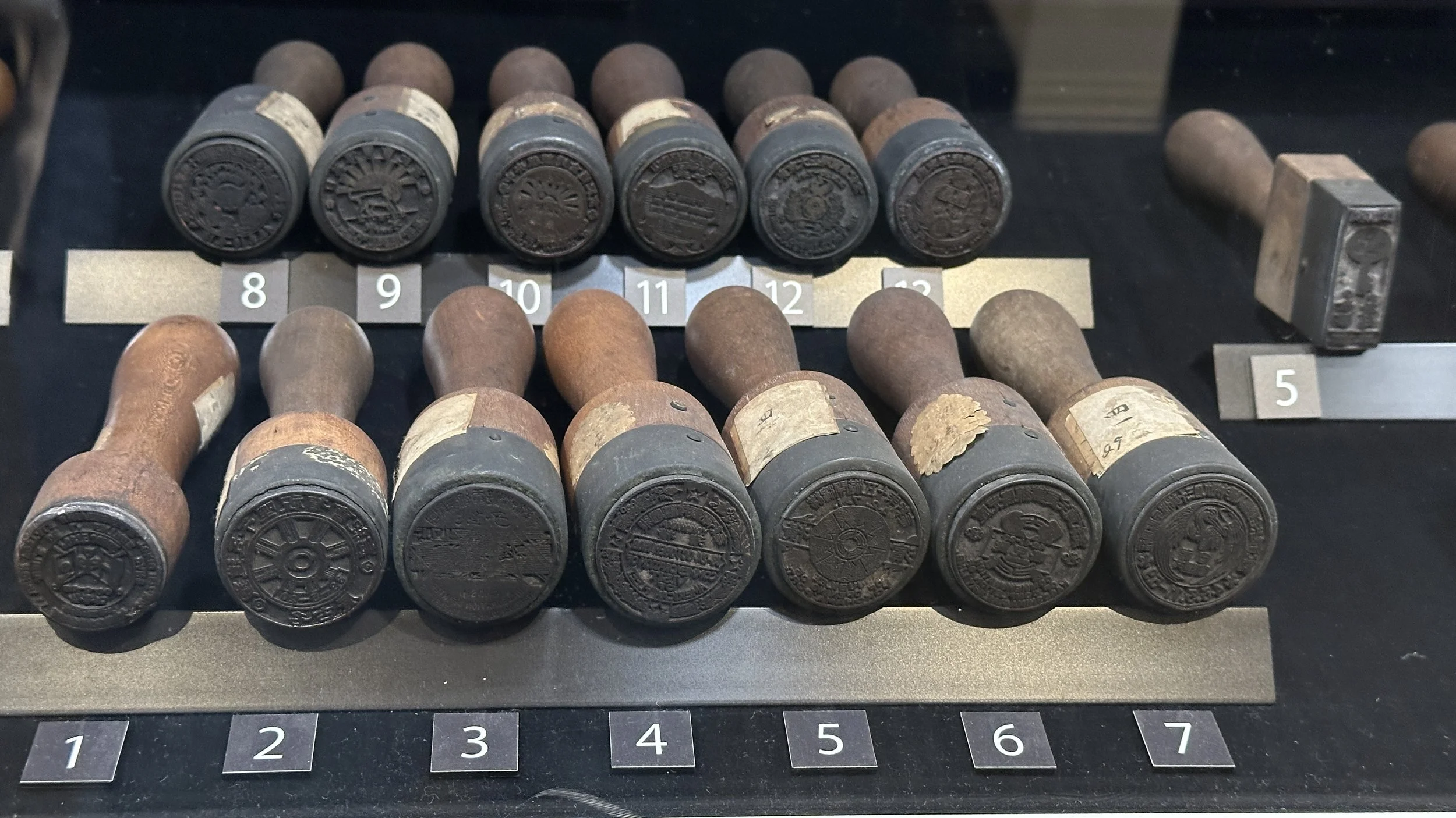 A series of cancelation stamps from the Japan postal museum is displayed in 2 rows so that viewers can see the bottom of the stamps