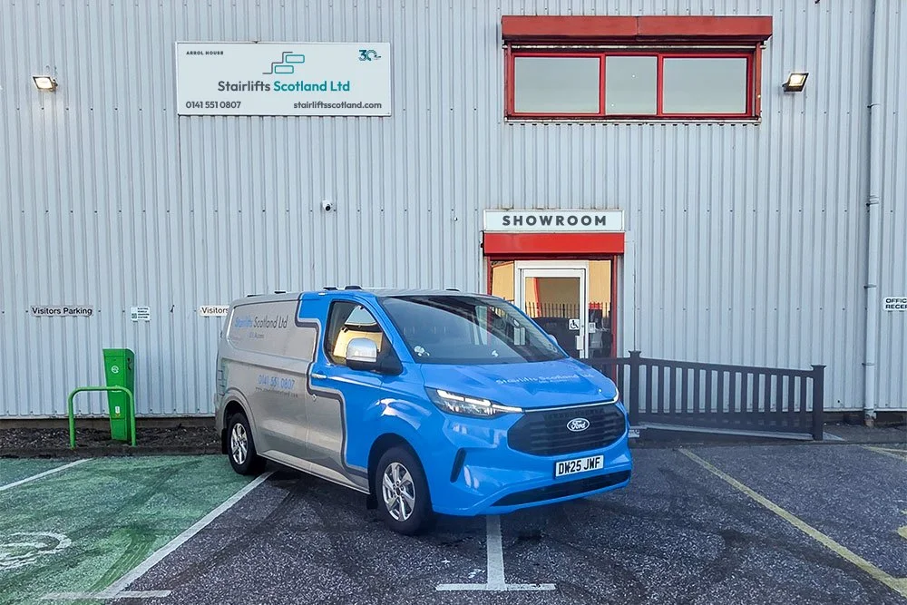A branded Stairlifts Scotland Ltd service van is parked outside the company’s showroom at Arrol House, which features a prominent accessible entrance ramp and designated disabled parking.