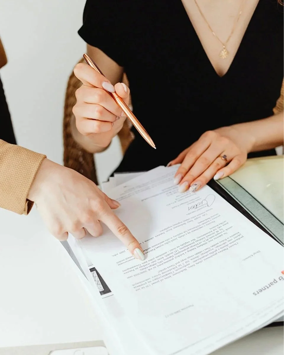 A close-up shot of two people reviewing a document, with one person pointing to a specific line of text while the other holds a gold pen.