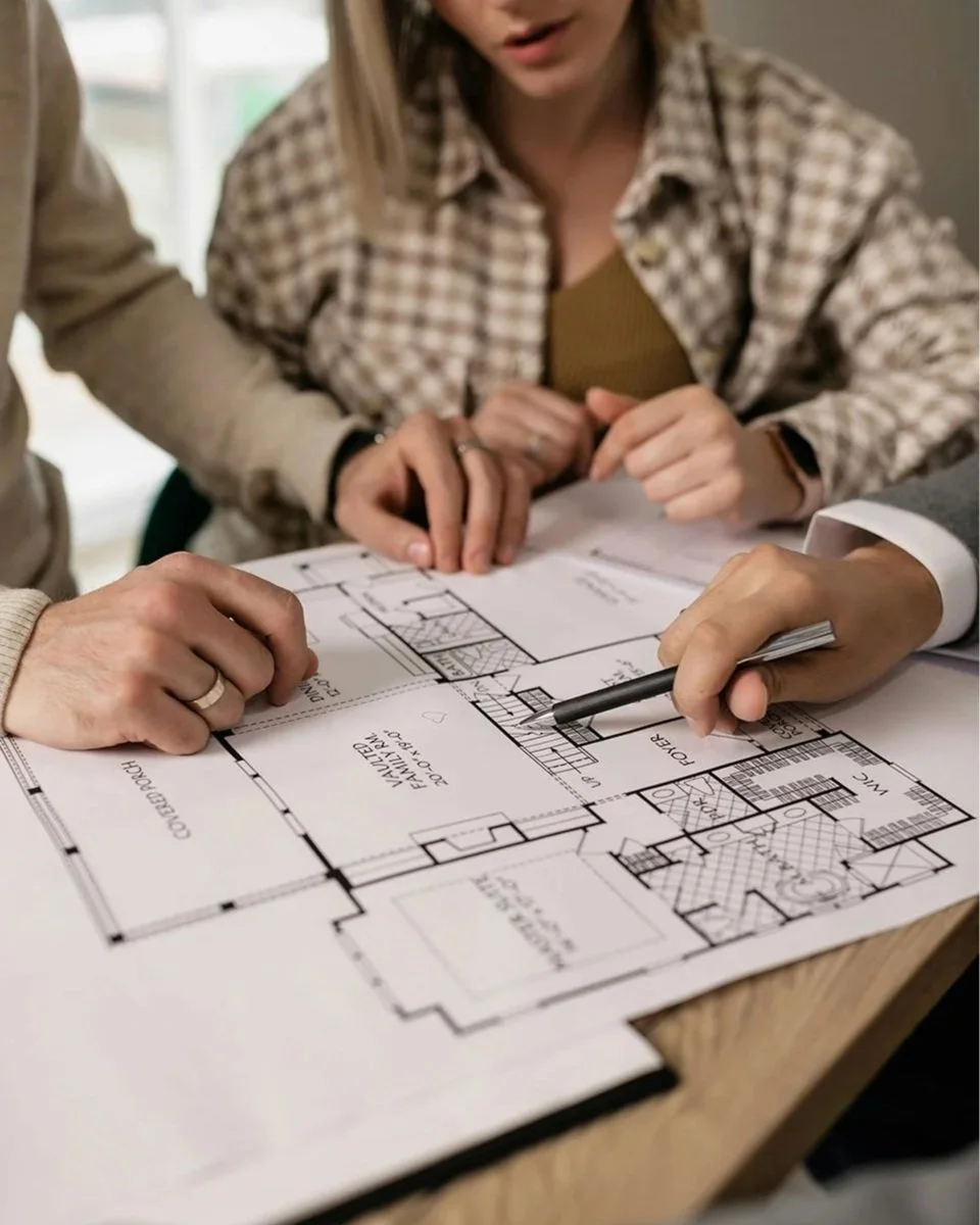 A consultant points a pen at a staircase on a detailed floor plan while reviewing home accessibility options with a client.