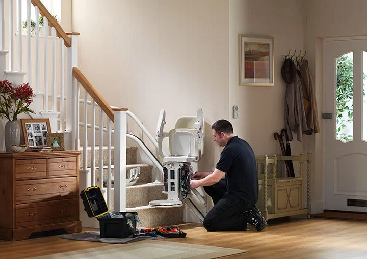 A Stairlifts Scotland engineer performing maintenance on a stairlift carriage installed on a home staircase.
