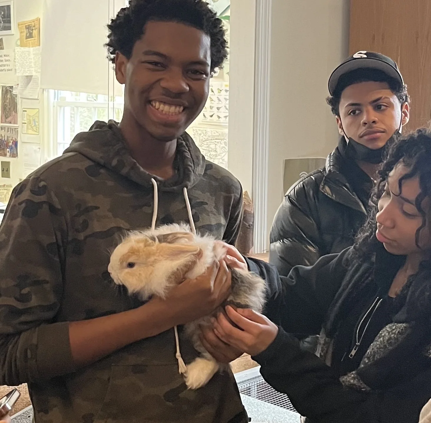 Three City to Sanctuary students holding a guinea pig indoors, during a nature-based learning program.