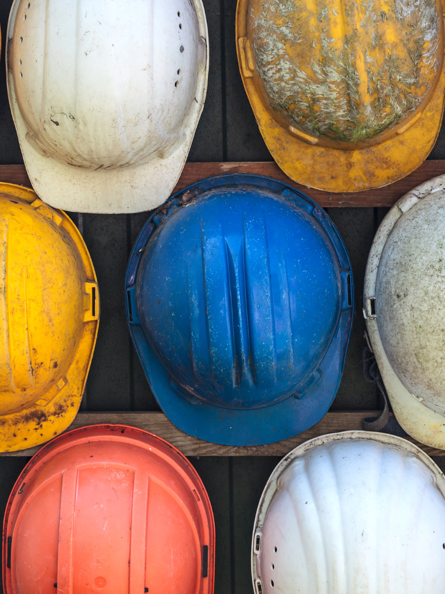 Top view of nine construction safety helmets in various colors including white, yellow, blue, pink, and orange, arranged on a surface.