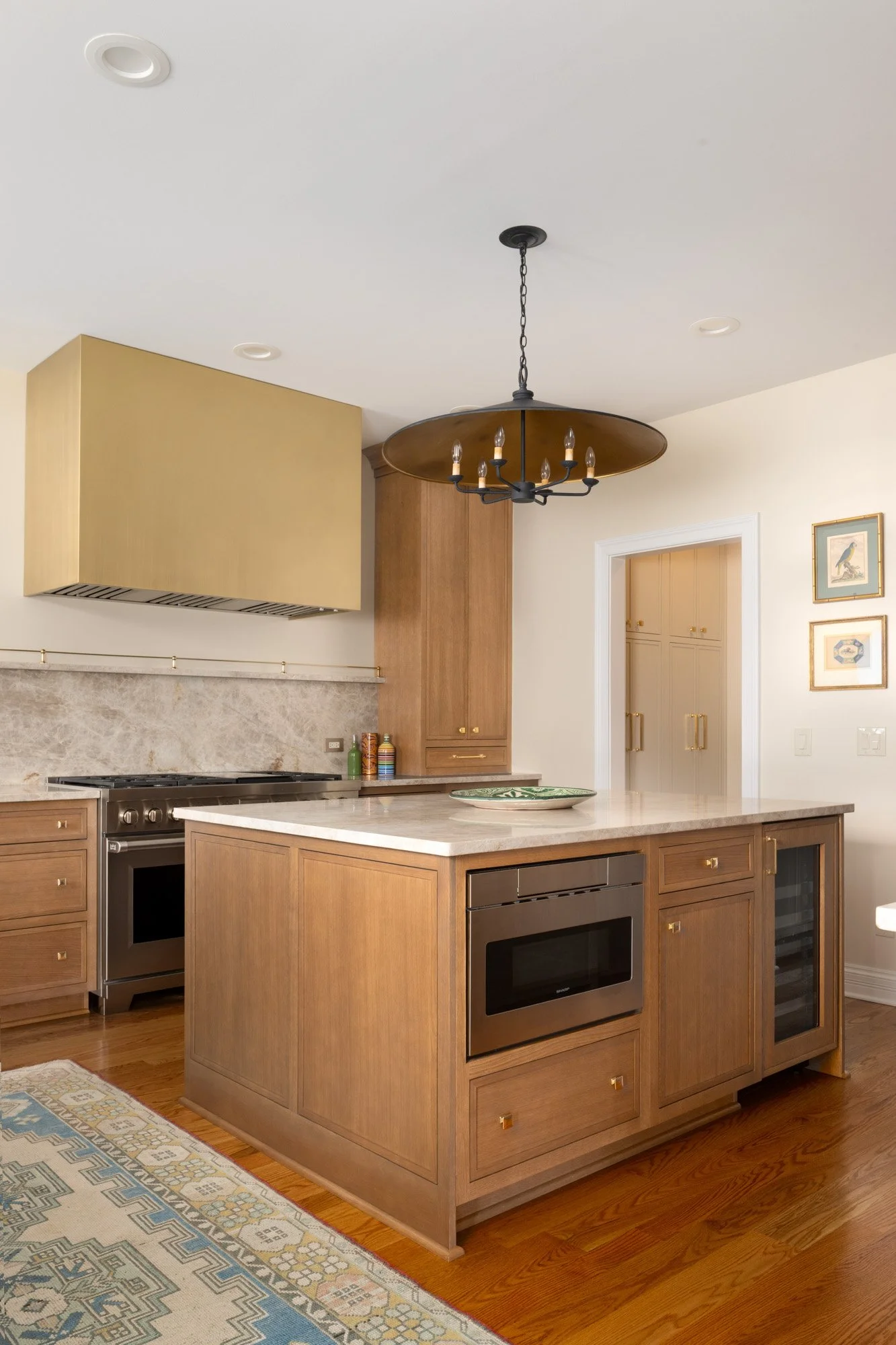 Kitchen with wooden cabinets, marble countertop island, stainless steel oven, and warmer, decorative chandelier, and framed pictures on the wall.