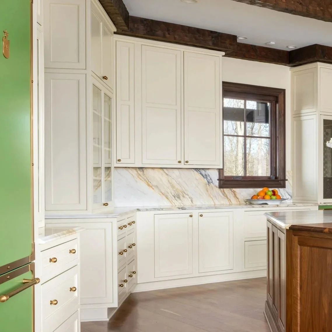 Kitchen with white cabinets, a marble backsplash, a window with a wooden frame, a bowl of oranges and apples on the counter, and a green refrigerator.