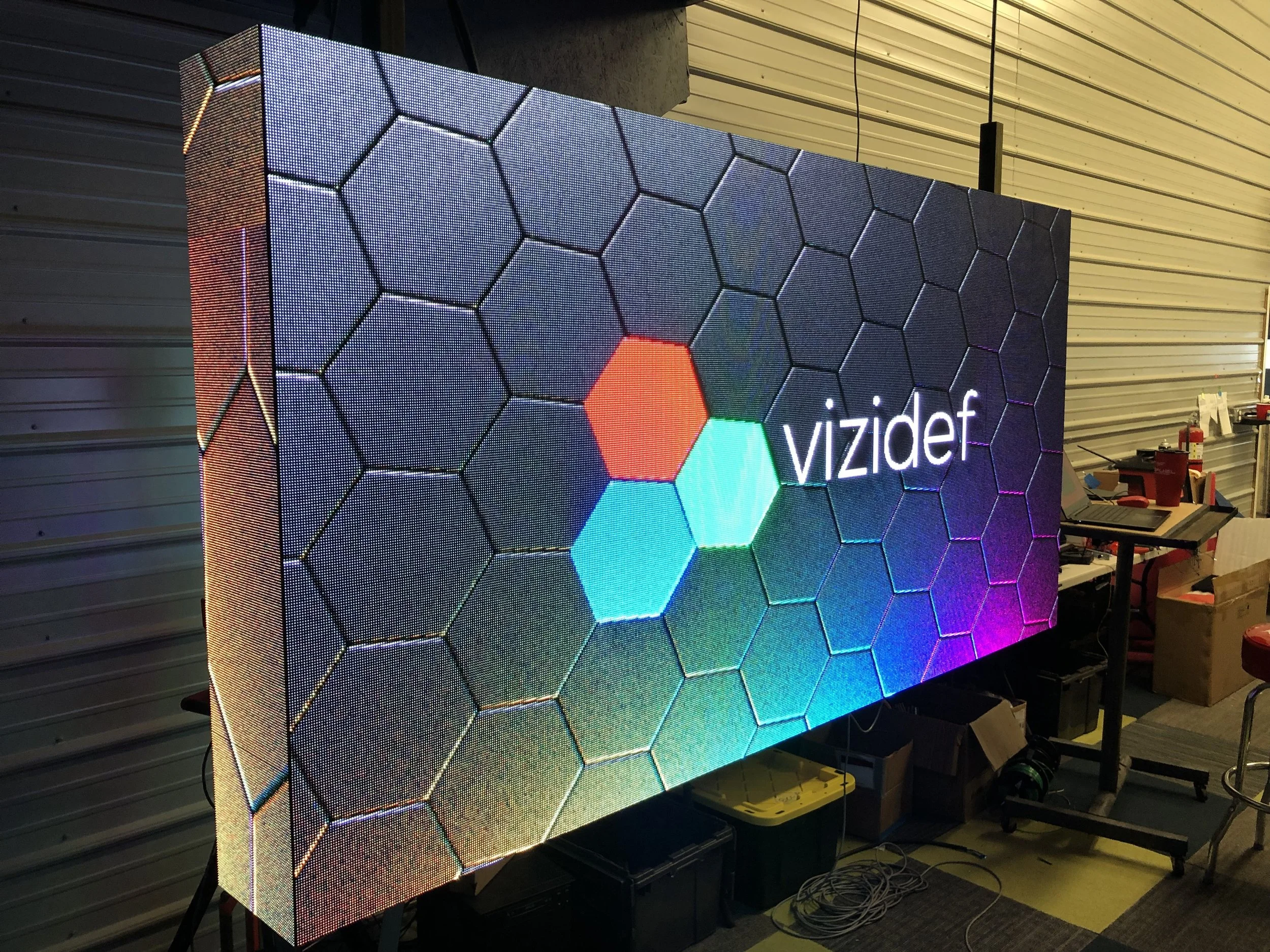 Large LED screen displaying the text 'vizidef' with a background of hexagonal patterns in various colors.