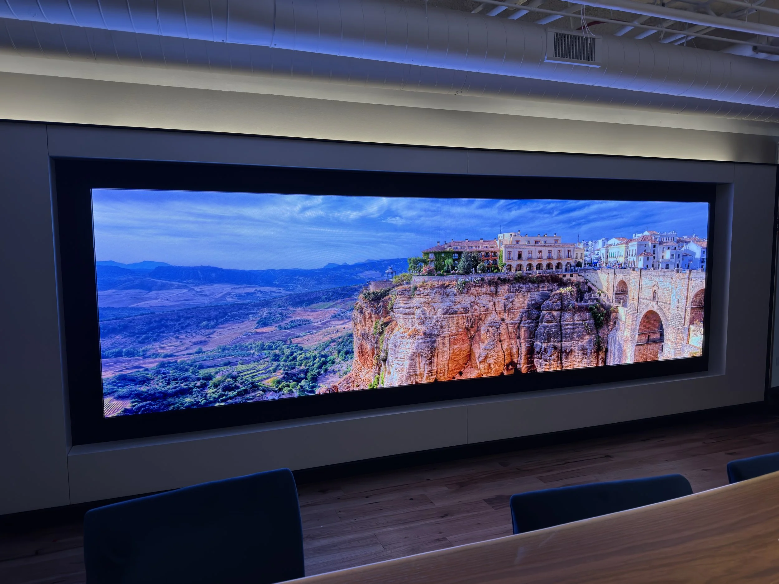A large digital display showing a scenic landscape of a city built on a cliff, with hills and mountains in the background, beneath a cloudy sky.
