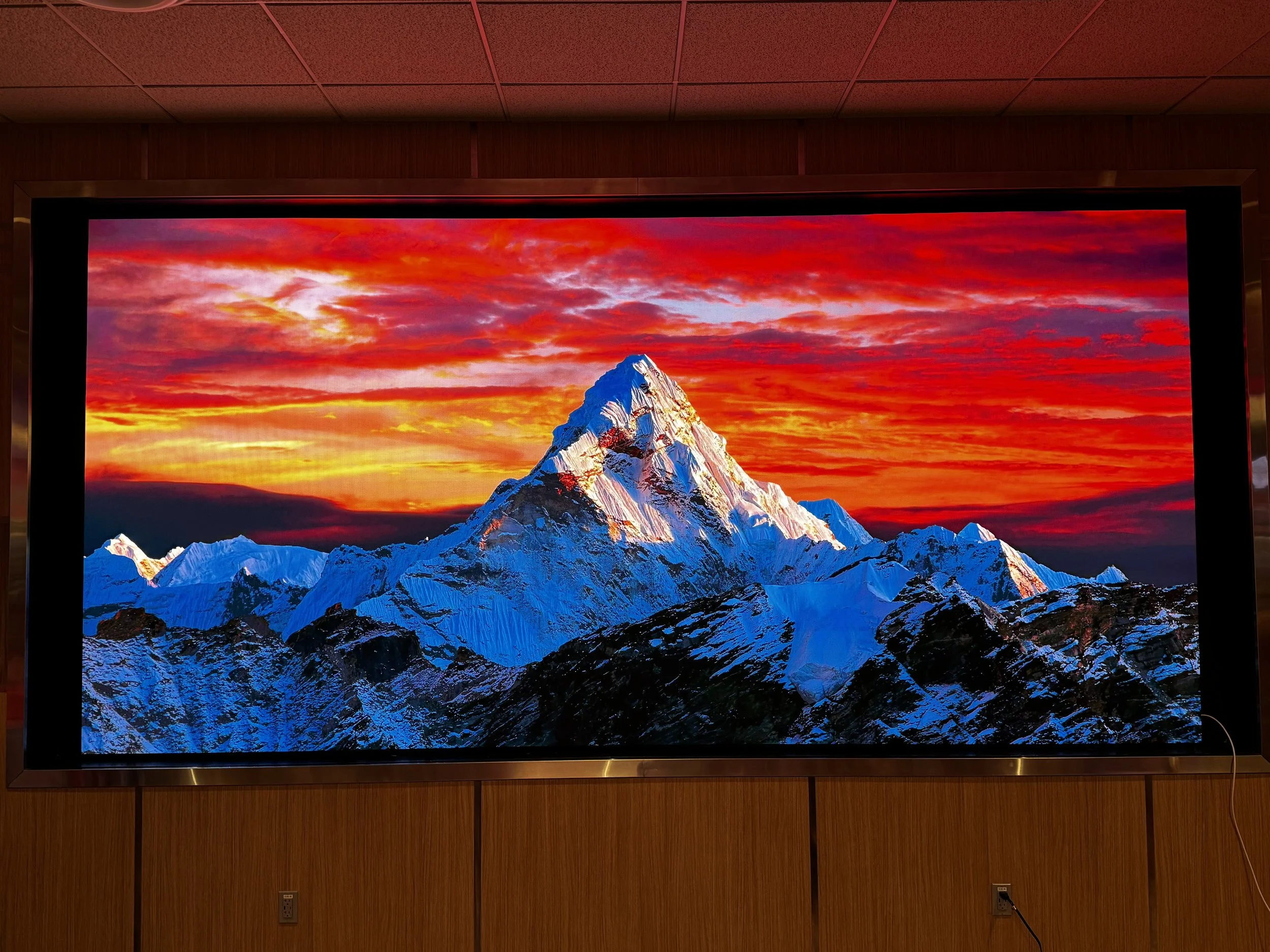 Large screen displaying a mountain with snow, set against a vivid red and orange sunset sky with clouds.