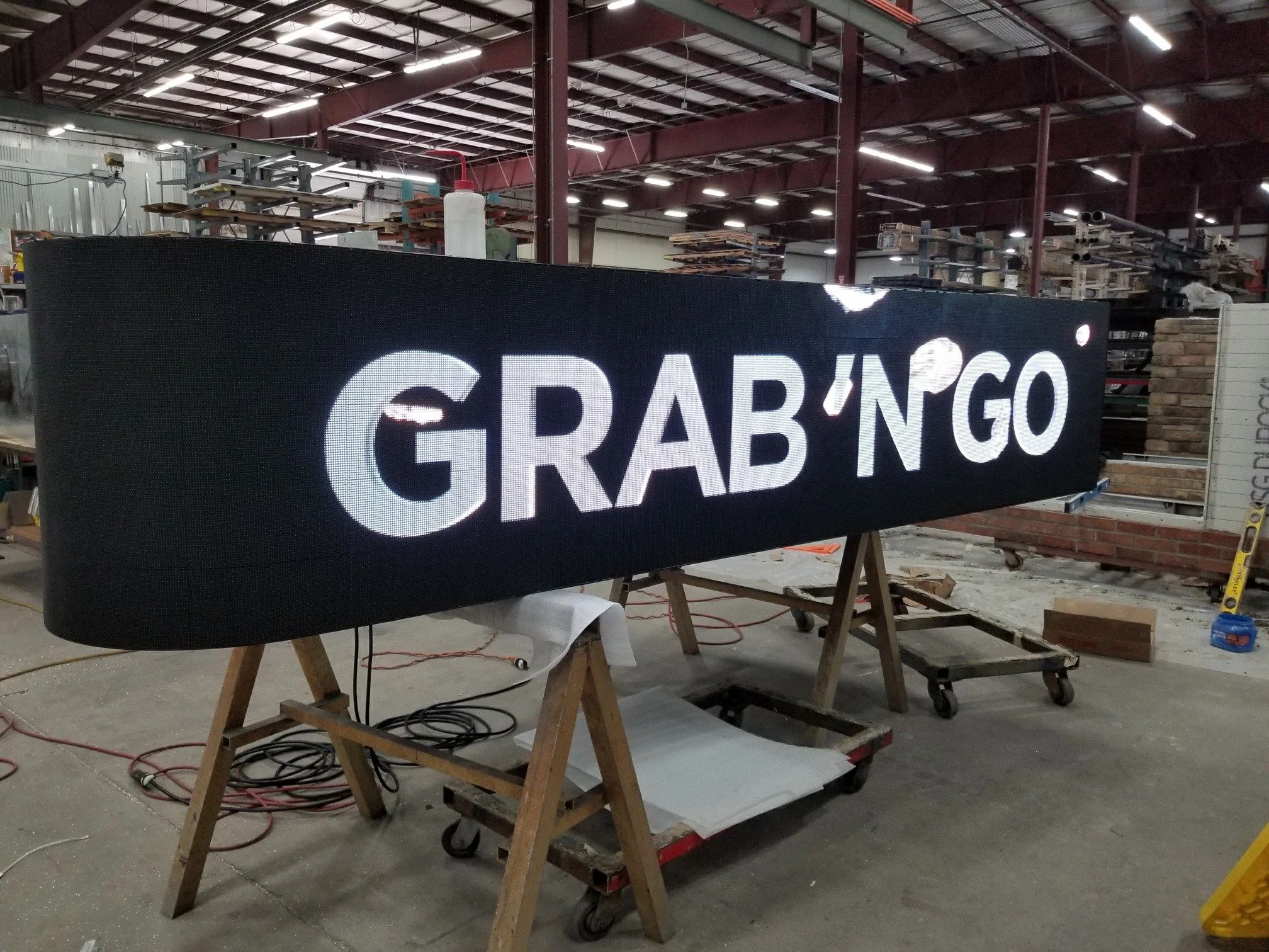 A large illuminated sign reading 'GRAB'N'GO' in white letters on a black background, located in an industrial workshop with tools and construction materials around.