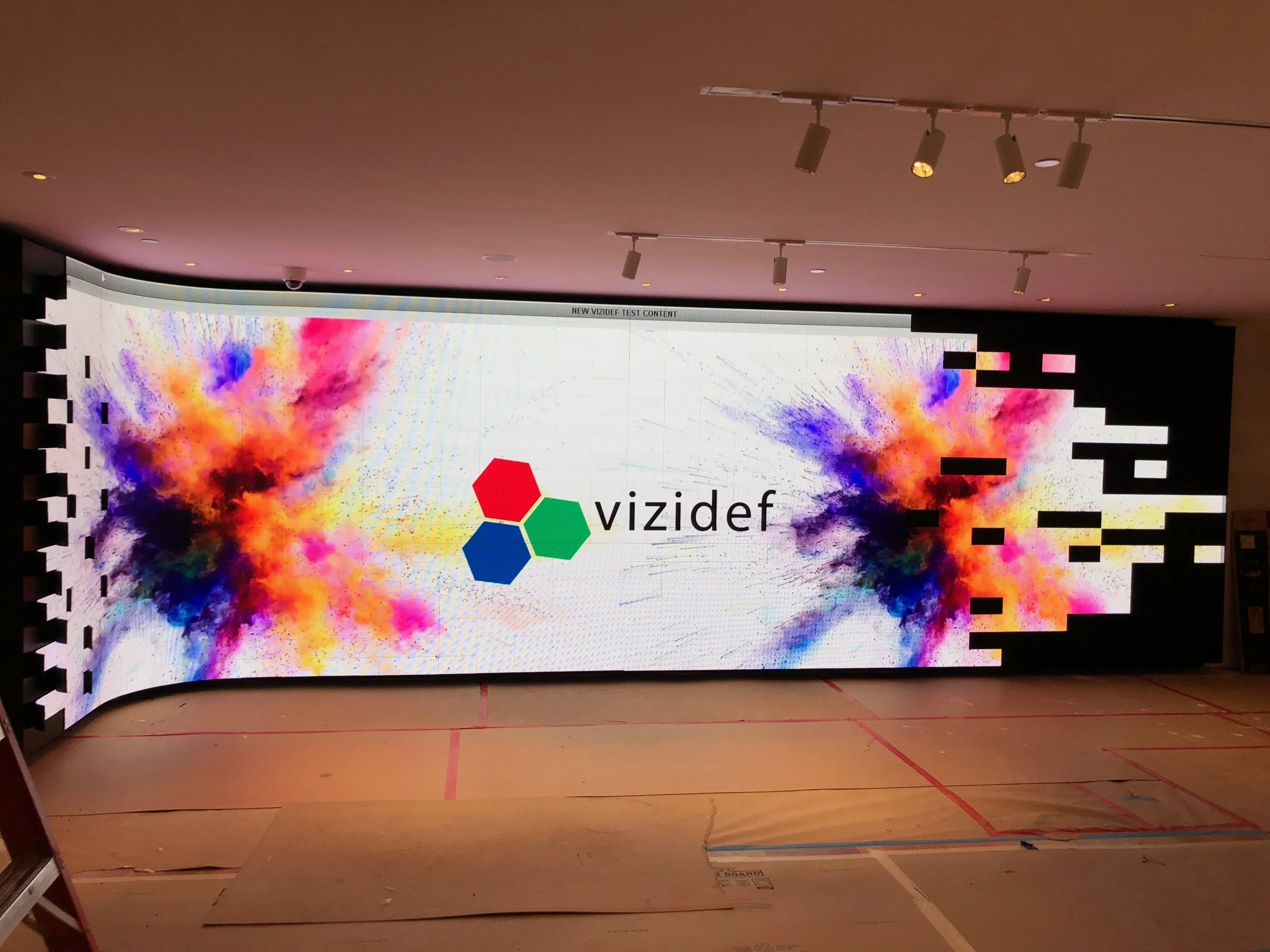 A digital display screen showing the logo of Vizidef, with colorful powder splashes on both sides.