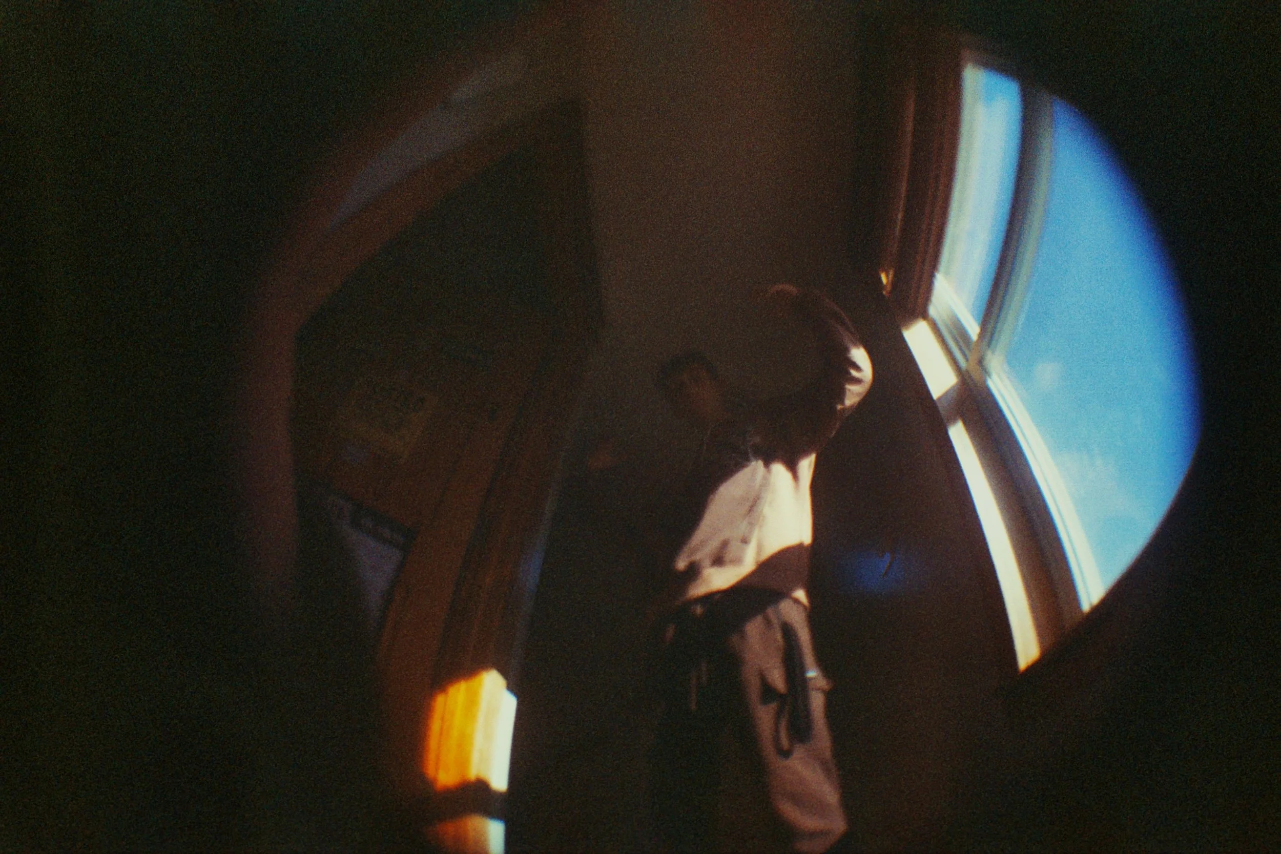 Person standing near a window with bright blue sky outside, seen through a circular peephole or fisheye lens.