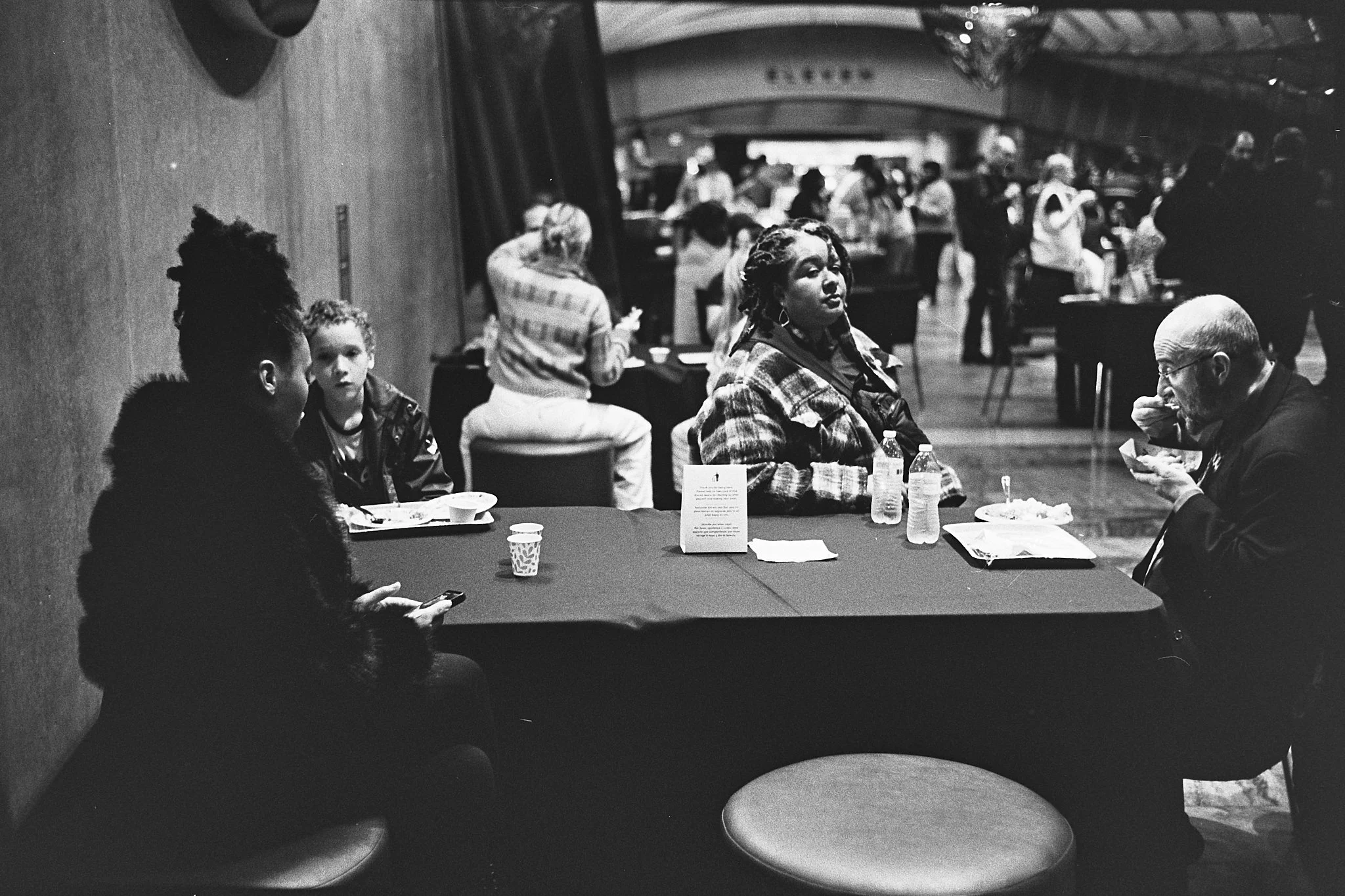 People sitting at a table in a busy indoor space, eating and talking.