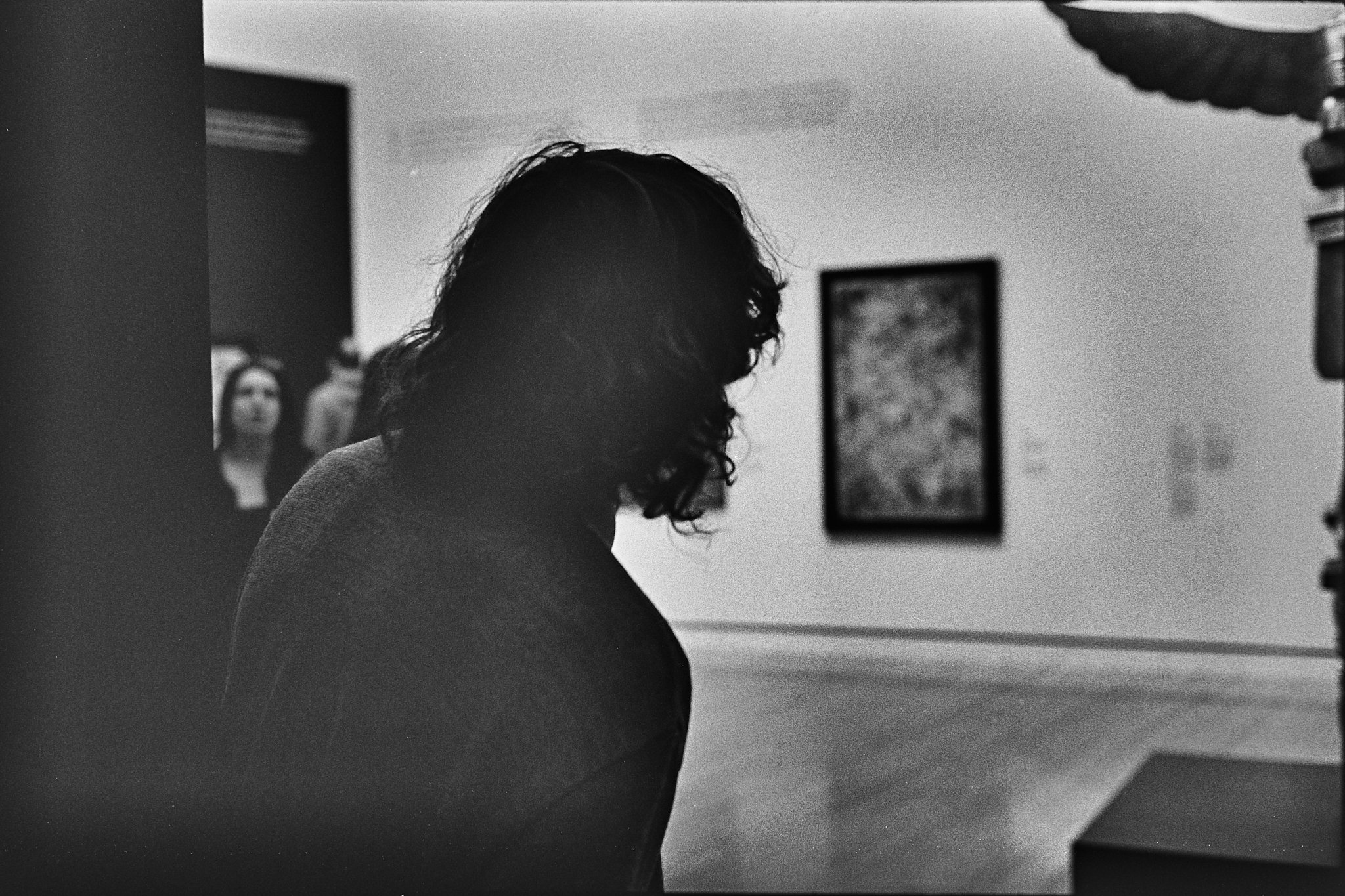 Silhouette of a person with long, curly hair in an art gallery, with artwork on the wall in the background.