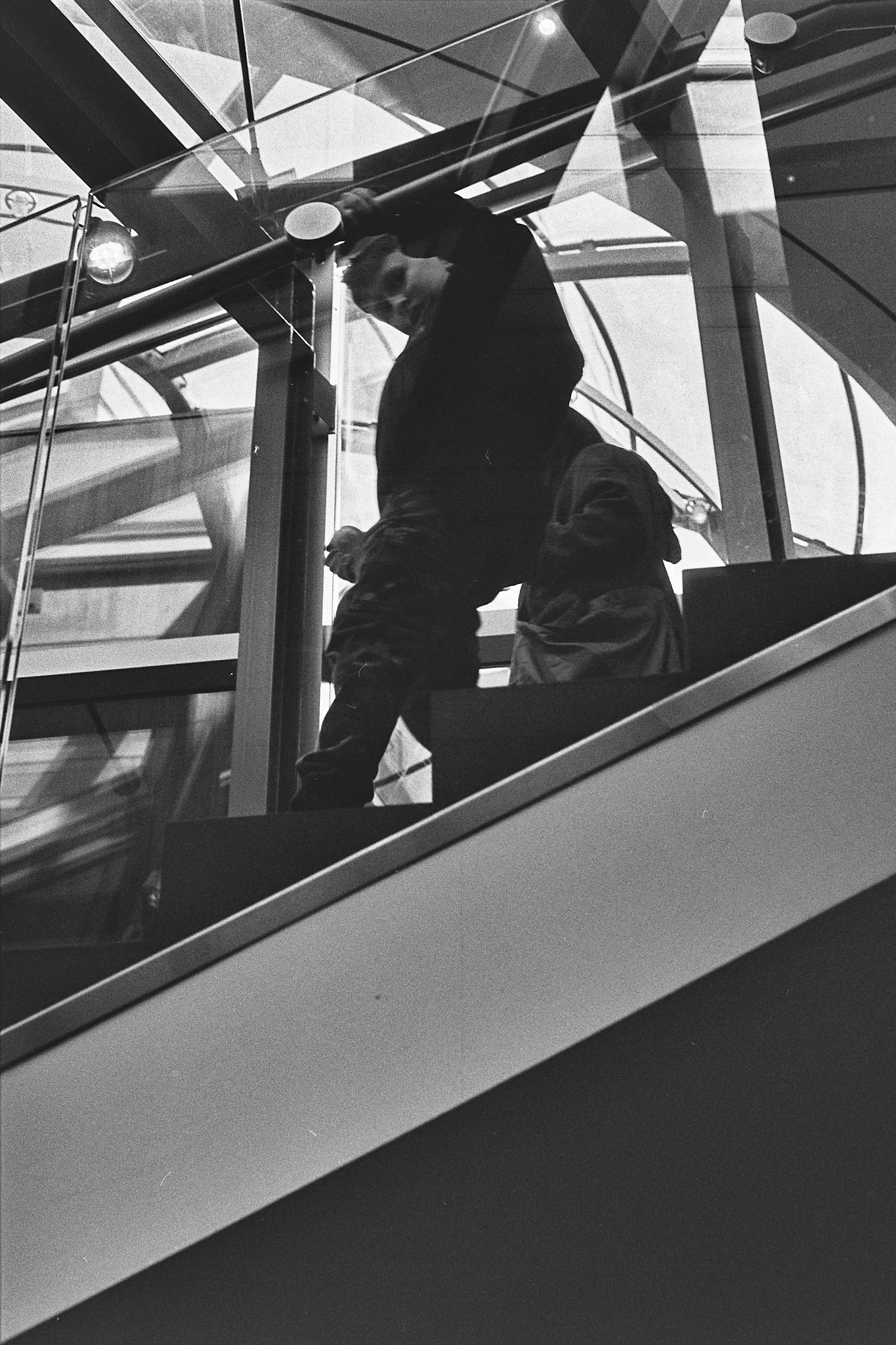 A man walking up an escalator inside a modern building with glass and metal architecture.