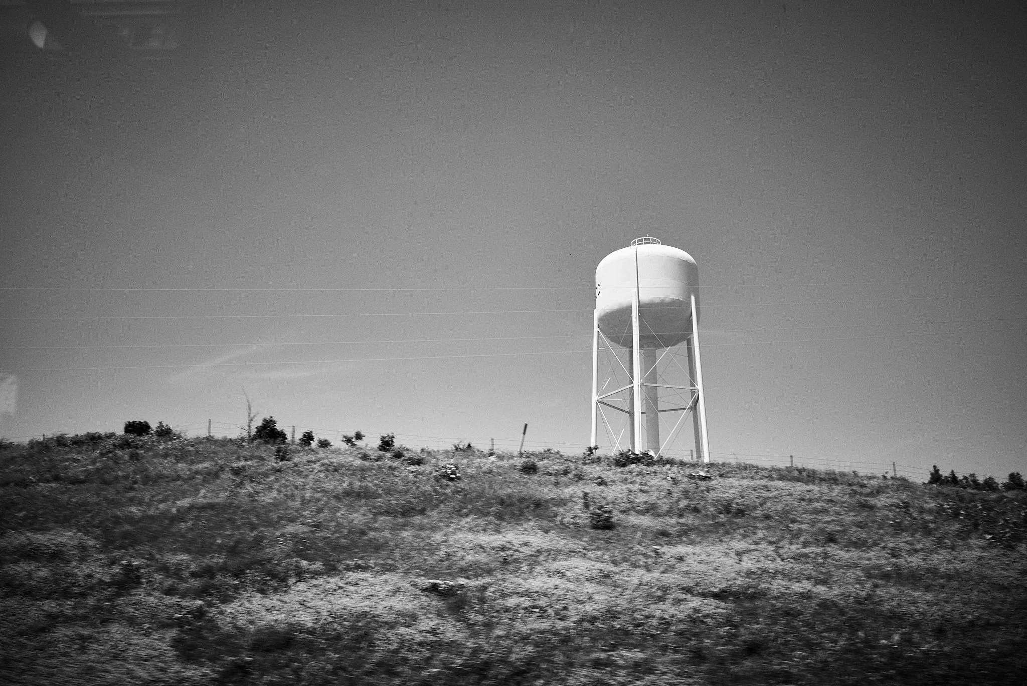 Black and white photo of a water tower on a hill with a clear sky in the background.