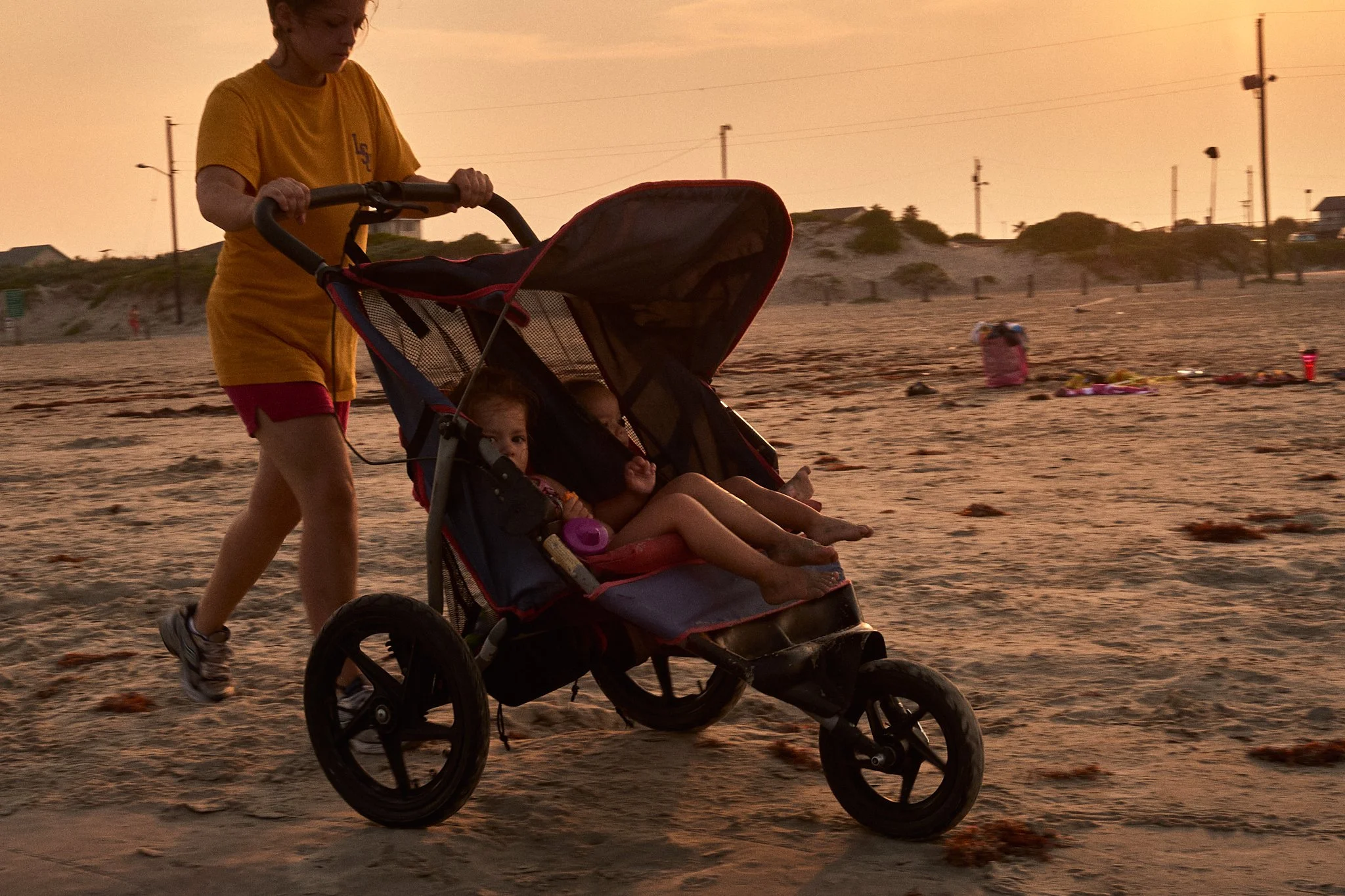 A woman pushing a stroller with two young children on a sandy beach during sunset.