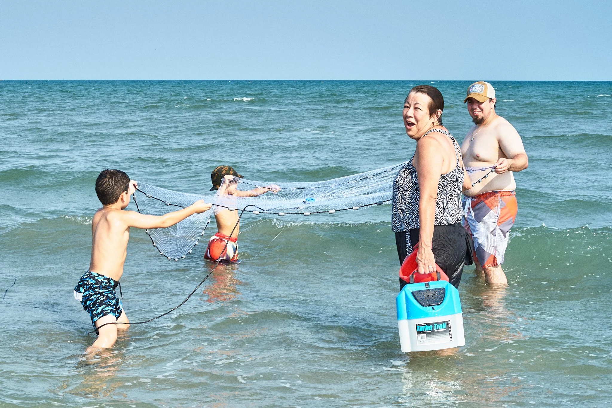 Family at the beach setting up a beach net in shallow water, with children and adults coordinating in the ocean.