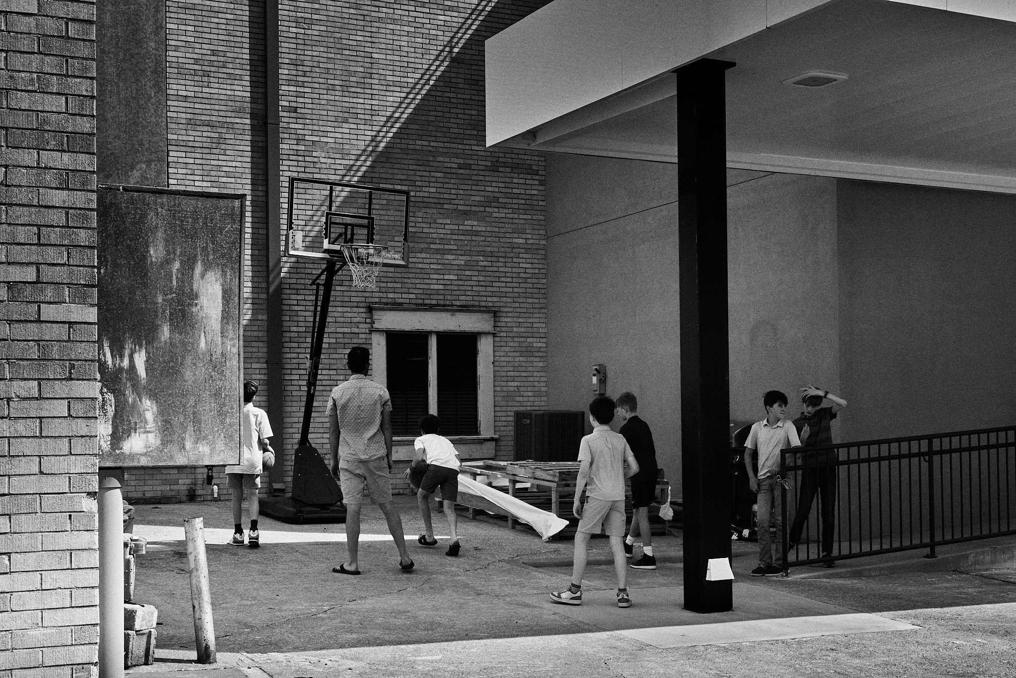 Children playing basketball outdoors on a concrete court near a brick building with a basketball hoop.