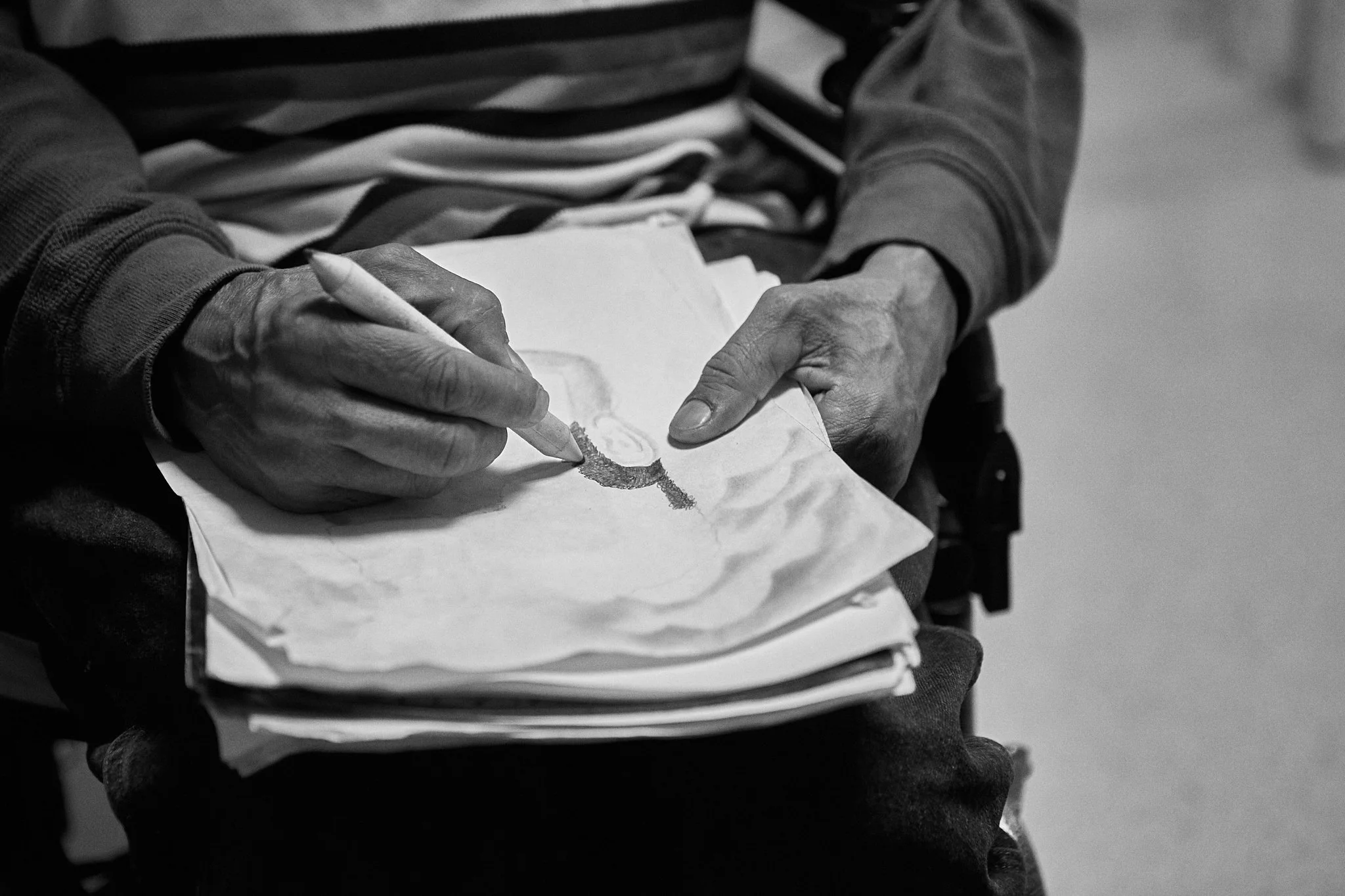 A person in a wheelchair is sketching a profile of a face on a piece of paper with a pencil.