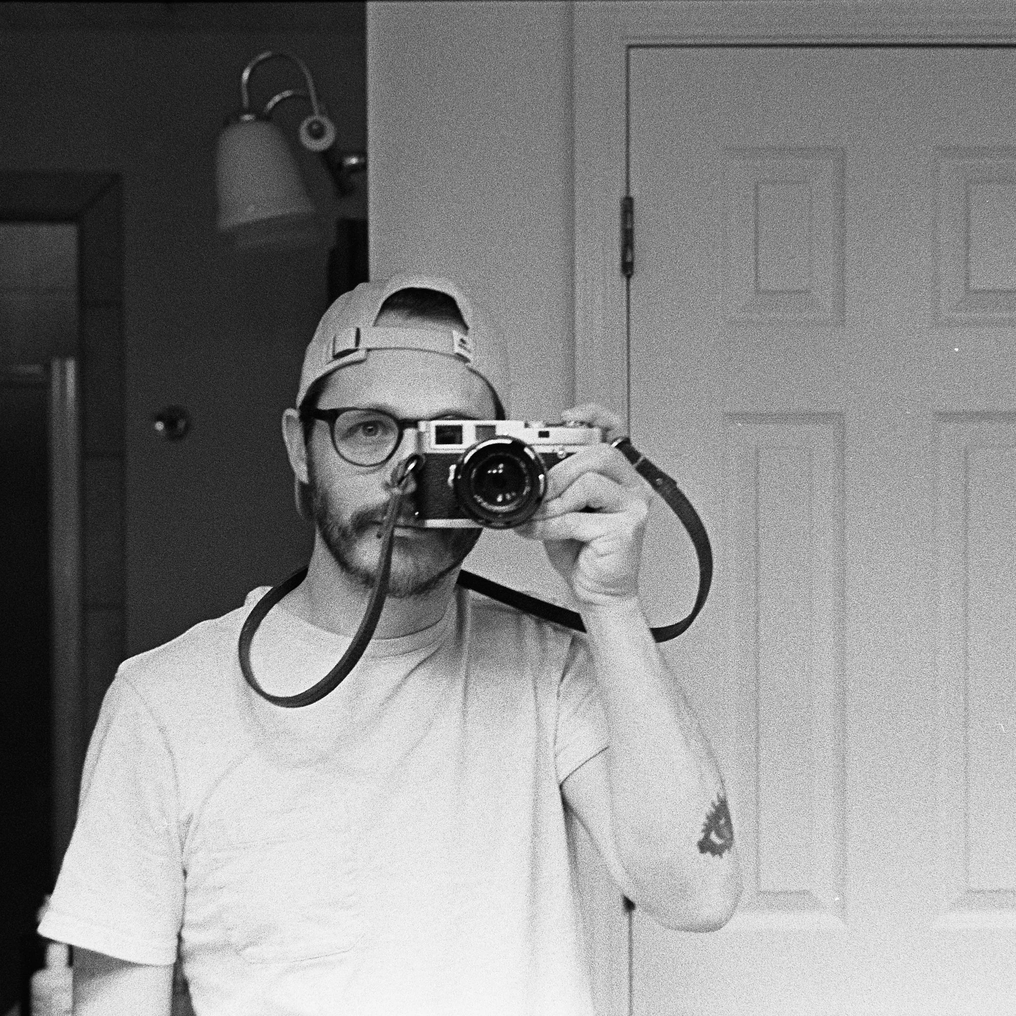 A man taking a selfie in a mirror with a vintage camera in black and white.