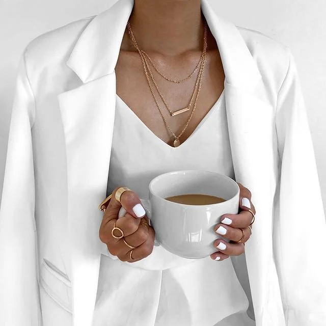 Person dressed in white holding a white cup of coffee or tea.