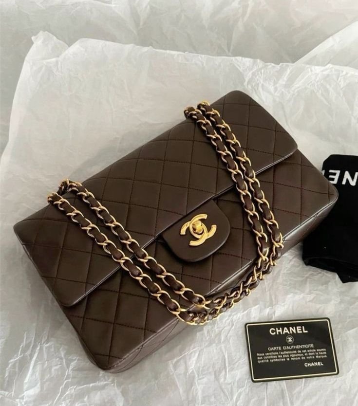 Brown quilted Chanel handbag with gold chain strap and gold CC logo, placed on white tissue paper with a black authenticity card nearby.