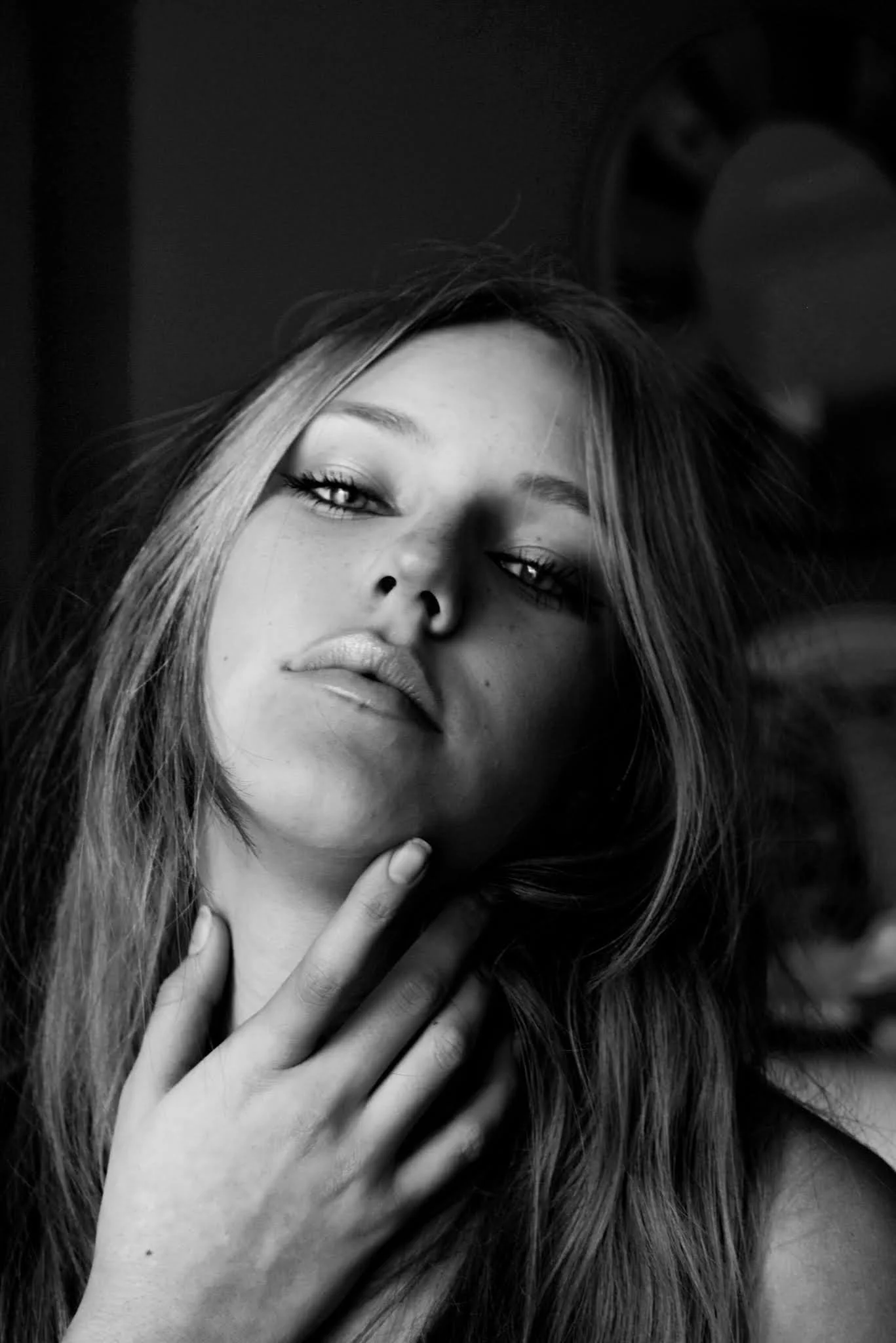 Black and white portrait of a young woman with long hair, looking at the camera with a relaxed expression, her hand resting near her chin.
