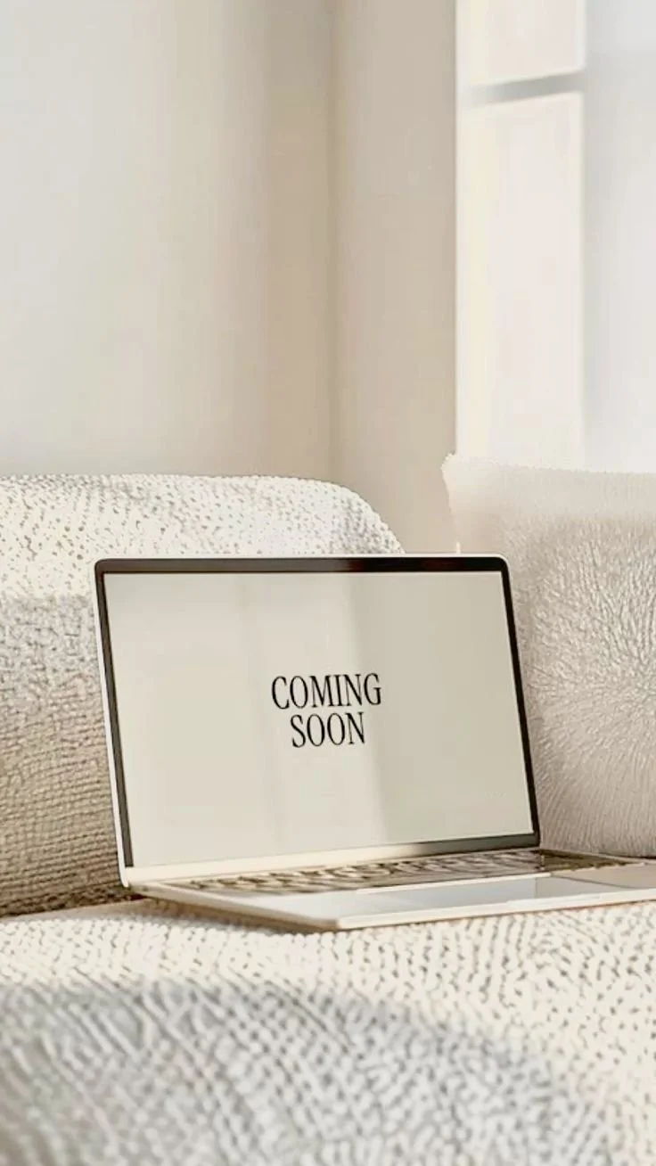Laptop on a white textured bed with a screen that reads "COMING SOON" in black text.