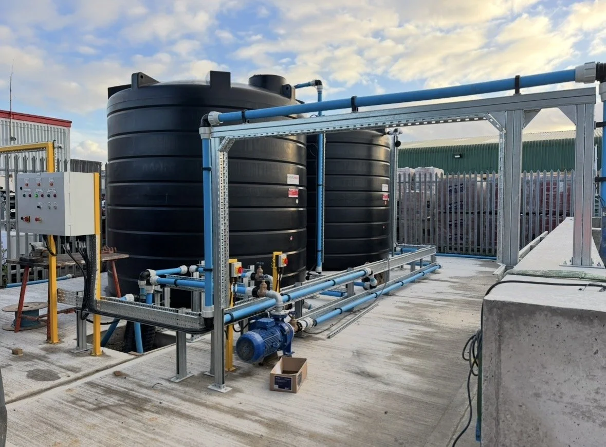 Industrial water storage tanks with piping and control panel on a rooftop or outdoor facility under a partly cloudy sky.