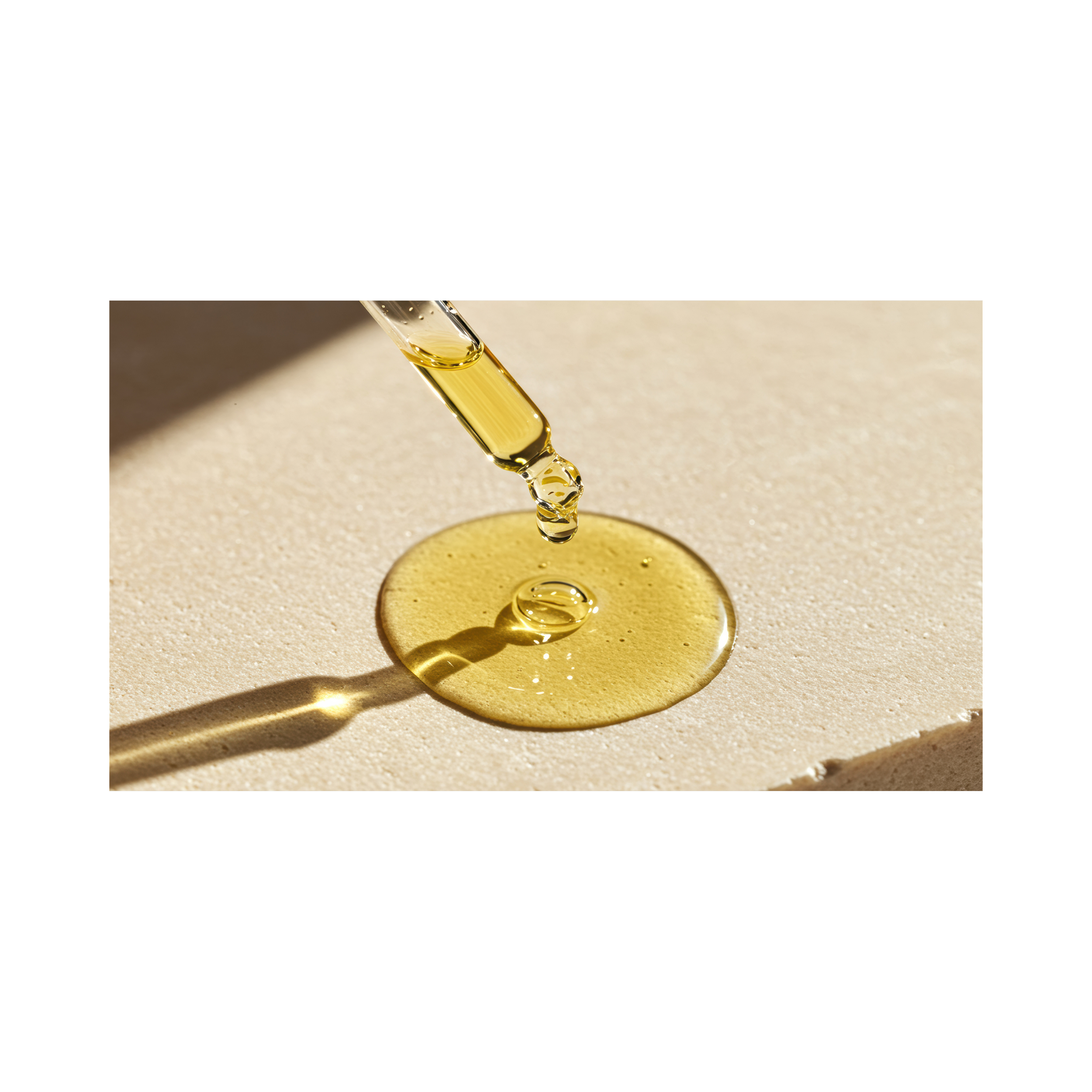 Close-up of a dropper releasing oil onto a circular pool of oil on a textured surface with sunlight casting shadows.