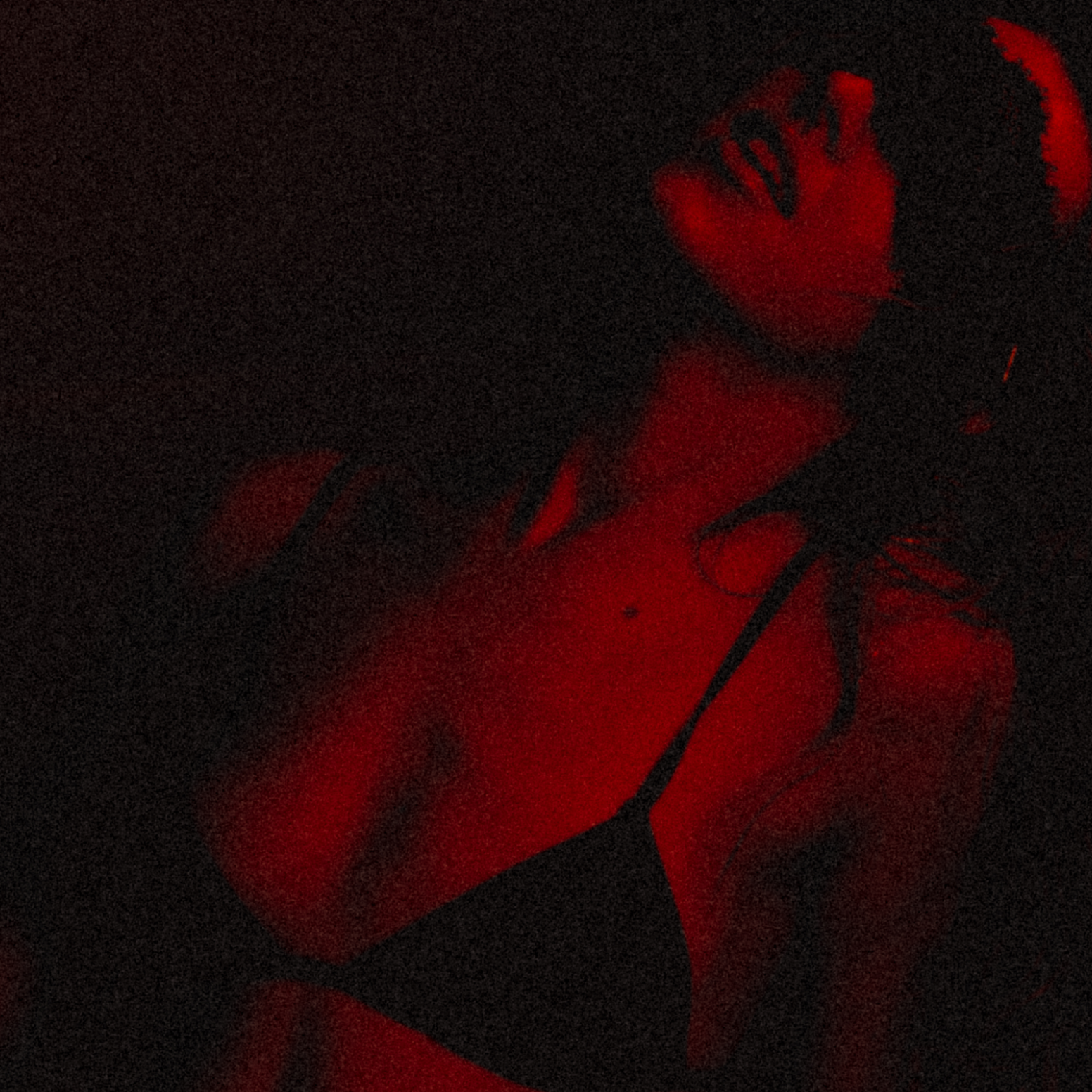 Claire De Lune is posing in a dimly lit environment with red-green lighting. She is wearing black lingerie and has long dark hair, with her head tilted back and face turned to the side.