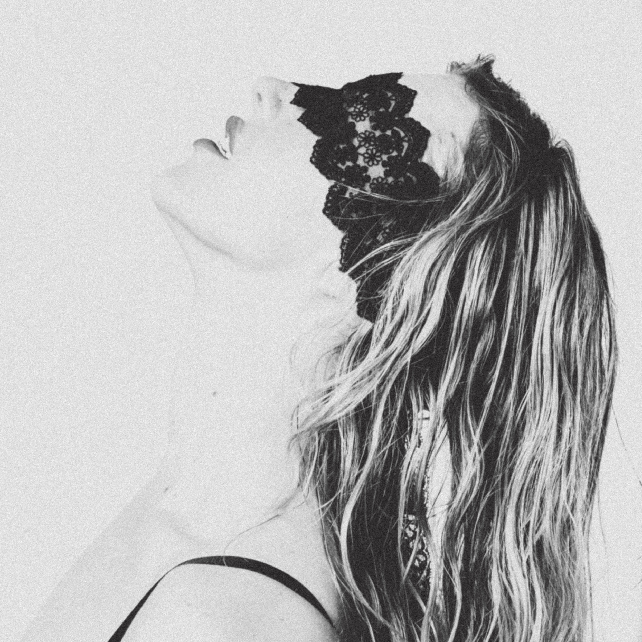 Claire De Lune with long, wavy hair wearing a black lace mask covering her eyes, facing left in a black-and-white photo.