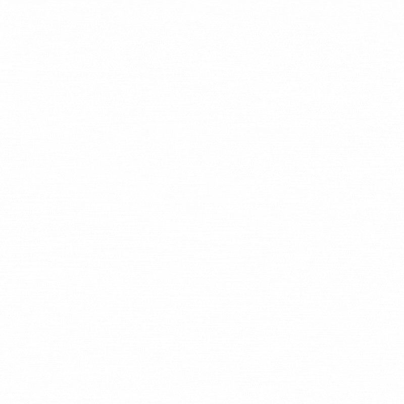 A black dog sitting on a grassy field at sunset with a sunset sky and trees in the background.