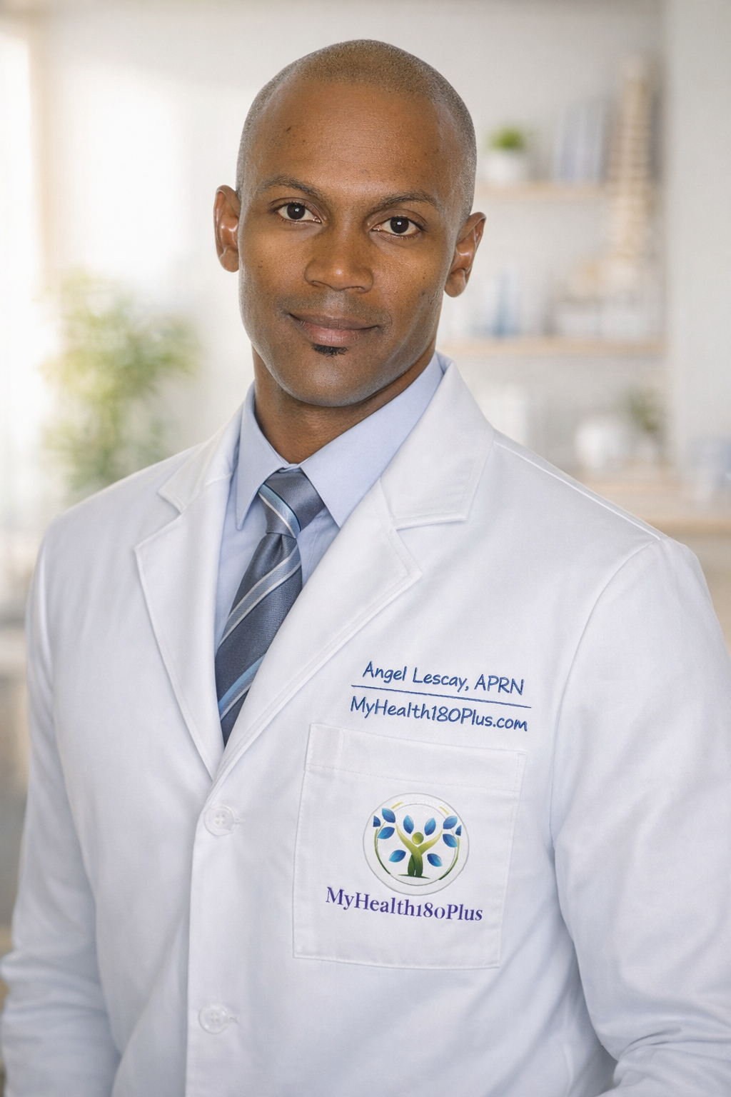 Portrait of a male healthcare professional wearing a white lab coat with the logo and name, in an indoor medical or clinical setting.