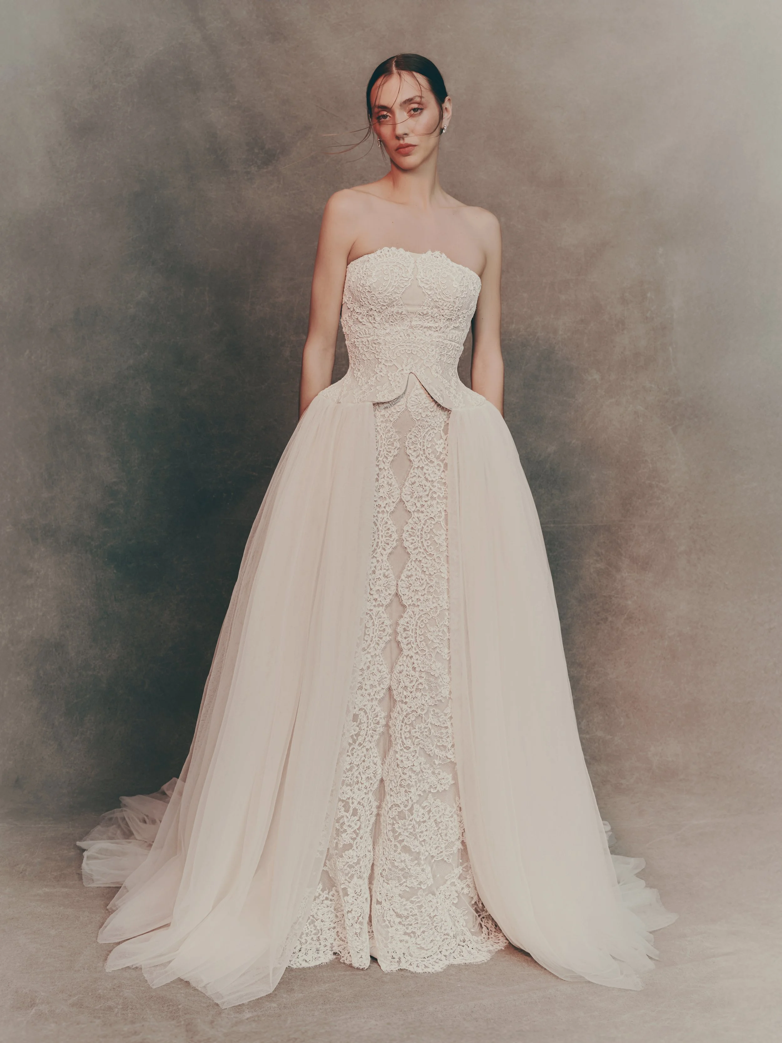 A woman wearing an elegant off-the-shoulder wedding gown with lace detailing and a full tulle skirt, standing against a neutral background.