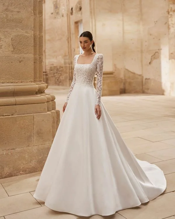 Bridal gown, voluminous silhouette. Made of mikado with a lace and beaded bodice. Square neckline, detachable sleeves, and round open back.