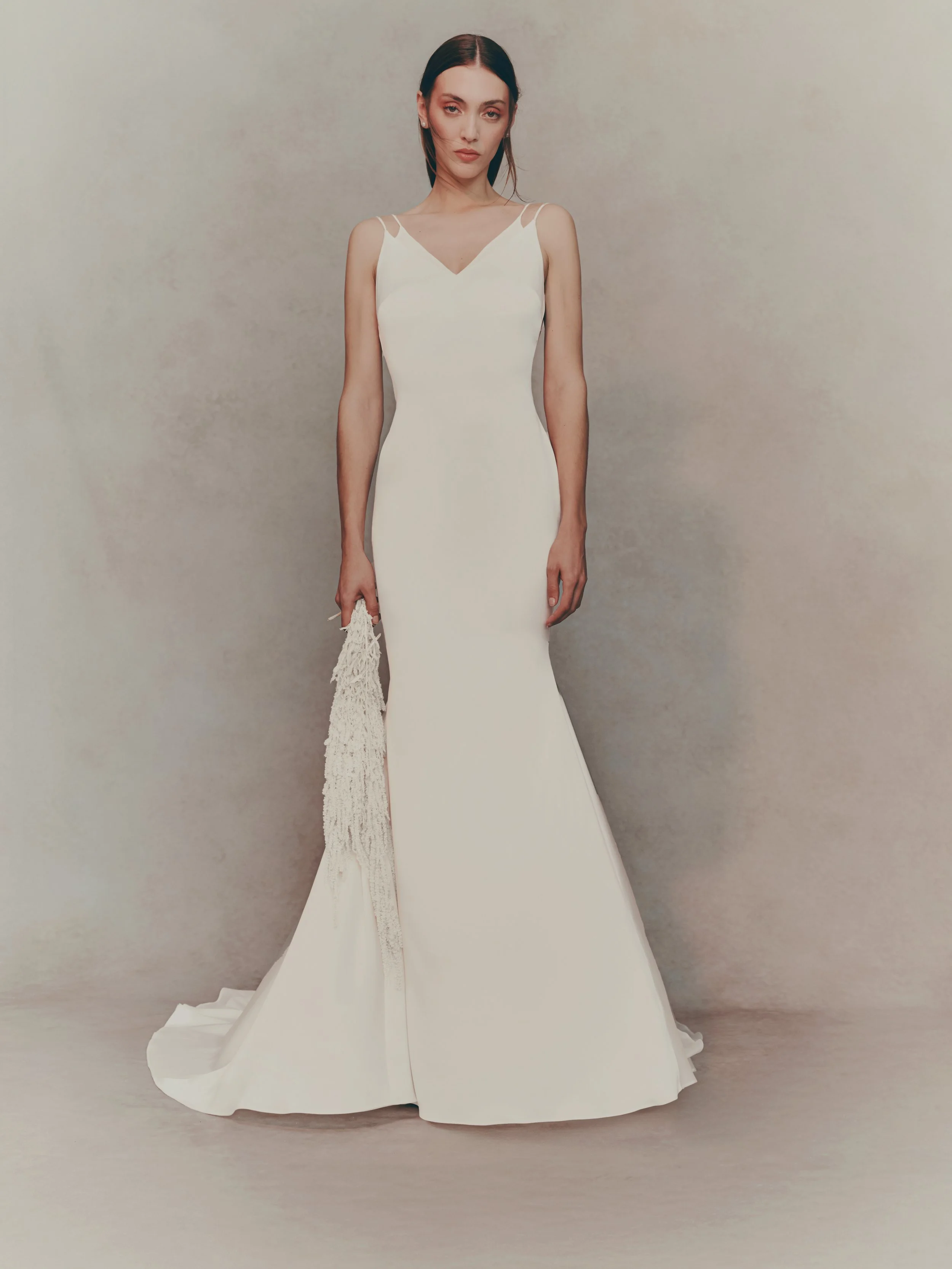 A woman in a long, elegant white dress holding a white lace handbag.