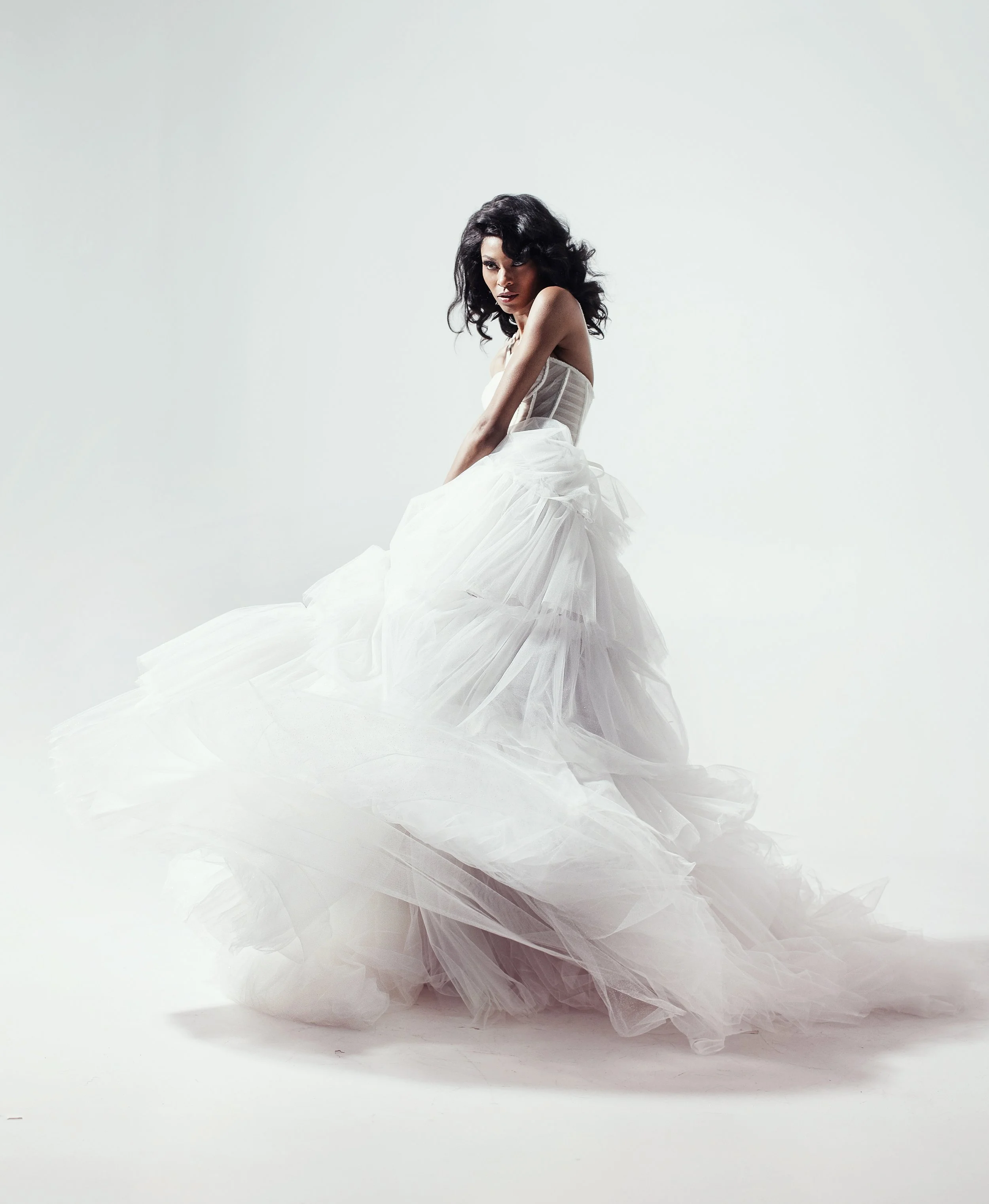 A woman in a voluminous white tulle dress poses against a plain white background.