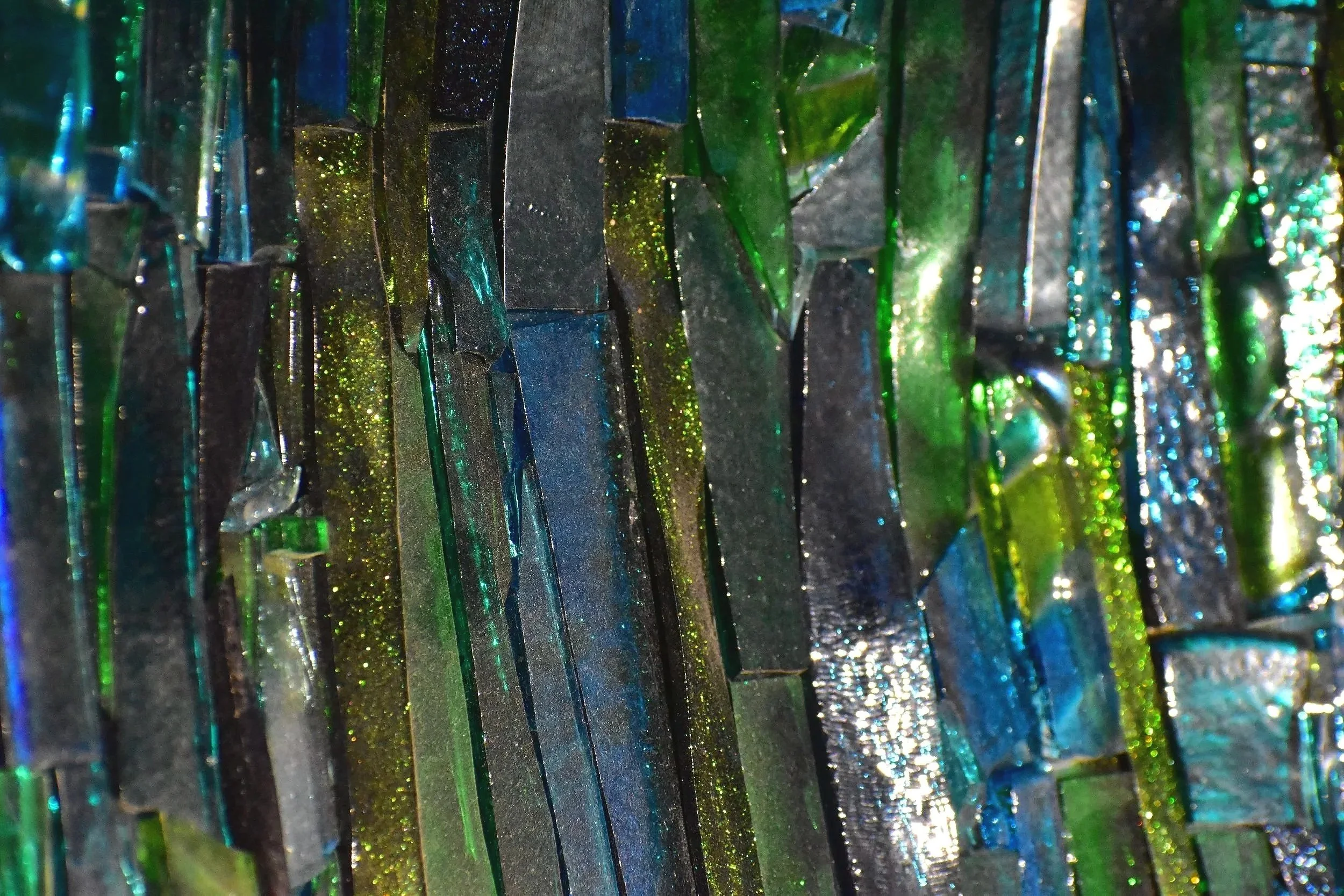 Close-up of shattered pieces of reflective glass or mirror in green, blue, and black colors.