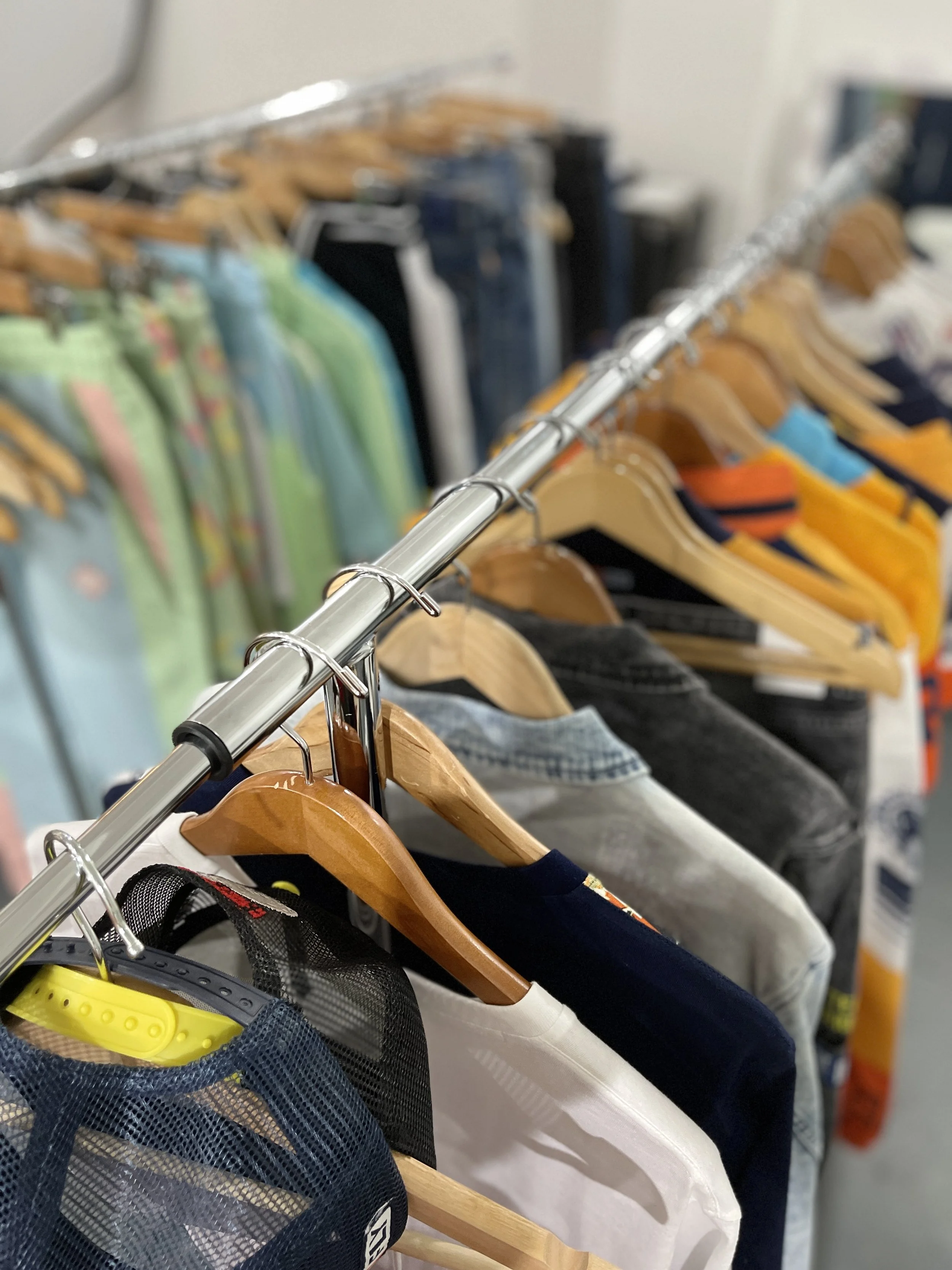 Clothing rack with various shirts and jackets on wooden hangers, some with colorful patterns and others in darker solid colors.