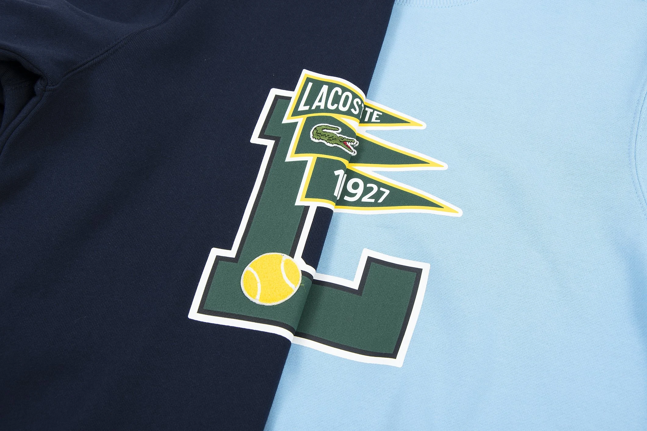 Close-up of a light blue and dark blue shirt with a Lacoste logo featuring a crocodile and the year 1927.