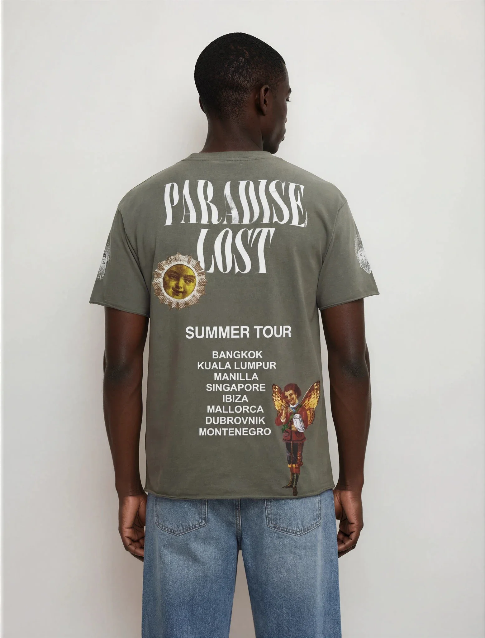 Back view of a man wearing a green T-shirt with text and graphics, standing against a plain white wall.