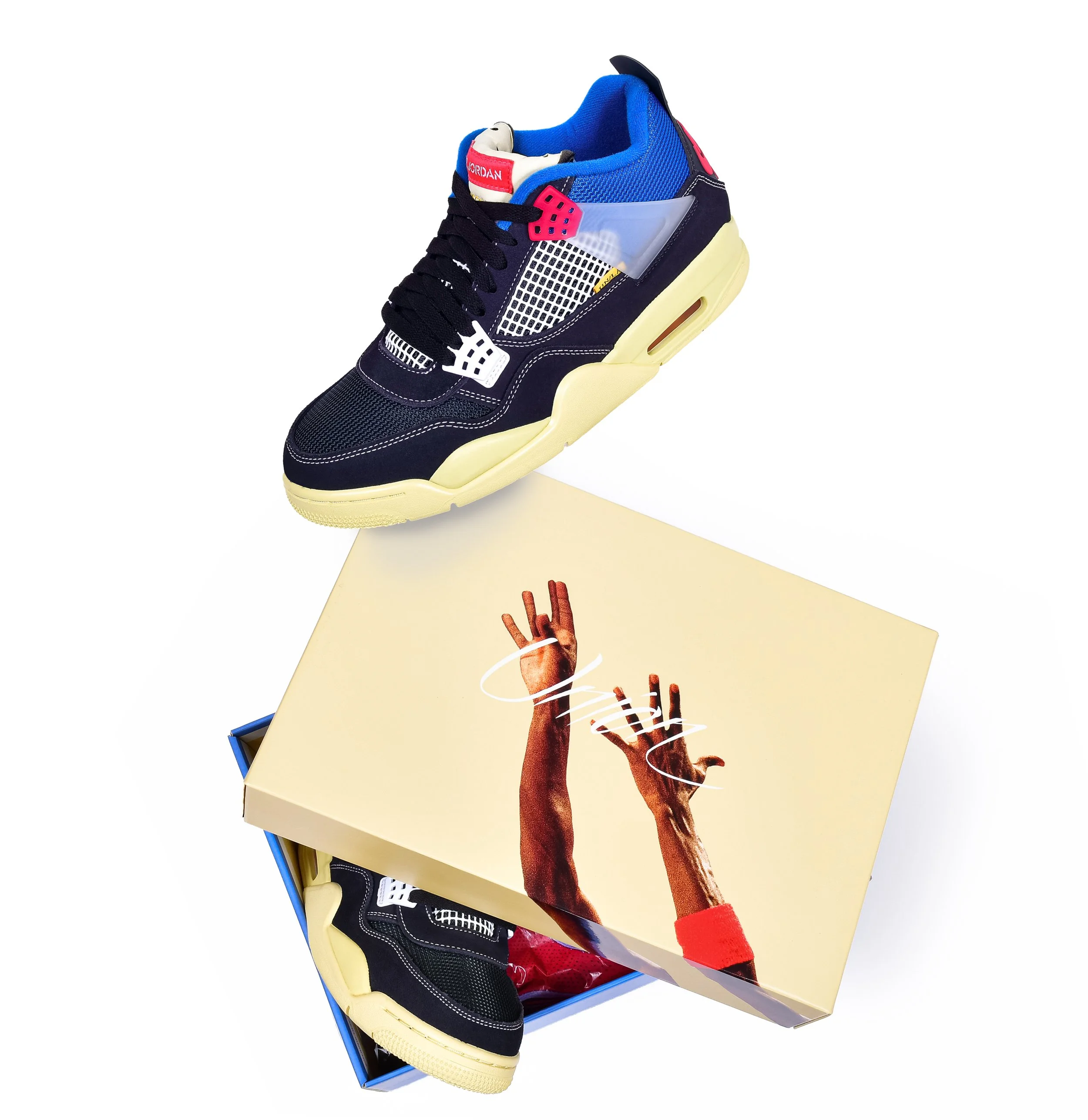 A close-up of a colorful sneaker, primarily navy blue with red, yellow, and white accents, displayed on a white surface and accompanied by a box with an artistic hand gesture printed on it.