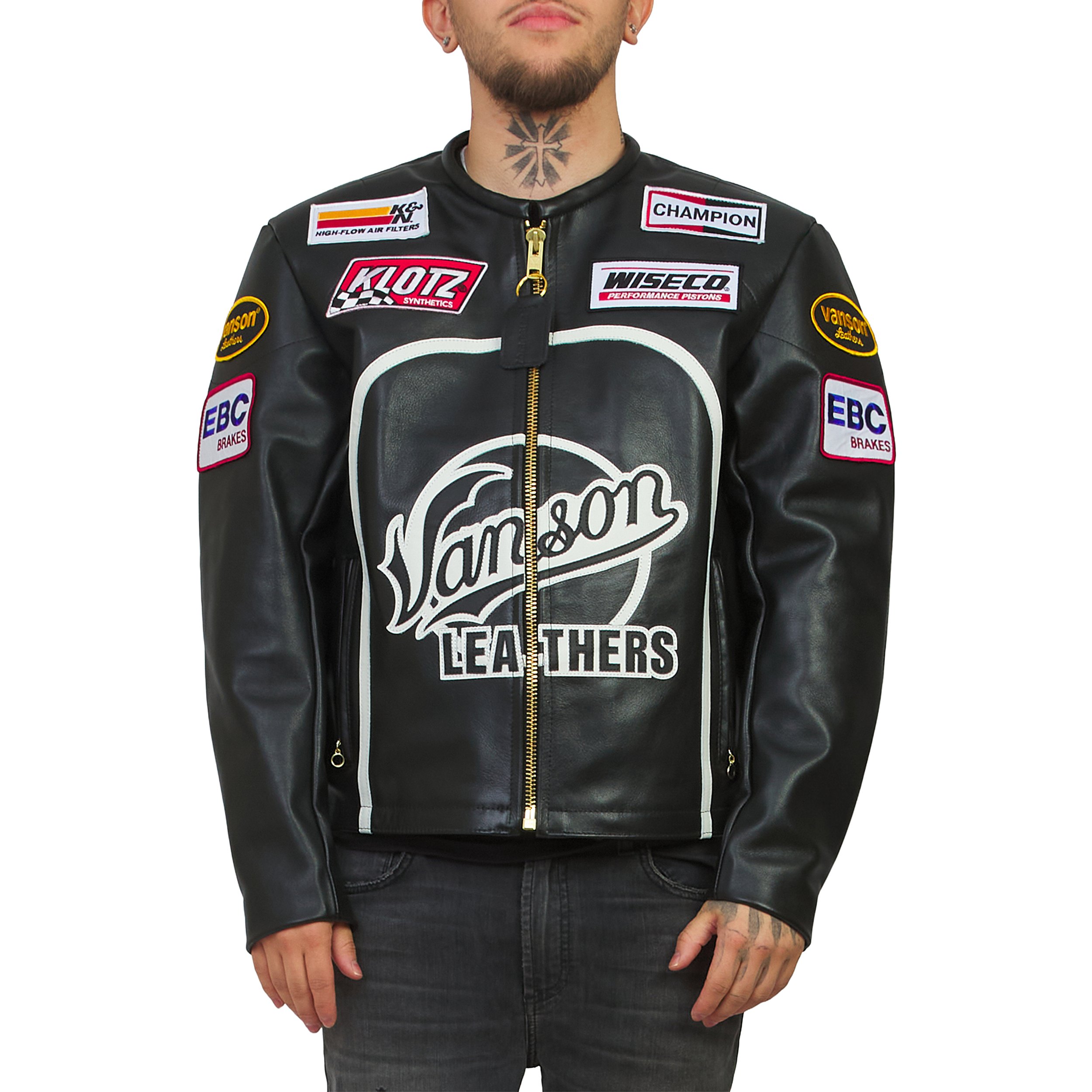 Close-up of a man wearing a black leather racing jacket with multiple sponsor patches, showing his neck tattoo and tattoos on his hands.