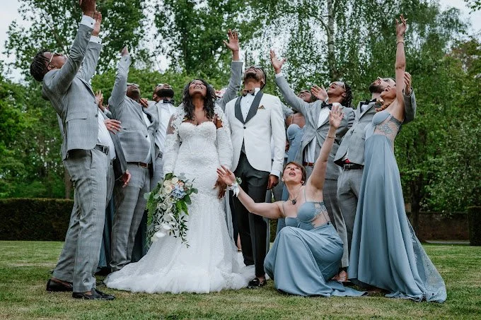A wedding party celebrating outdoors, with the bride and groom at the center, surrounded by friends and family raising their hands and celebrating.